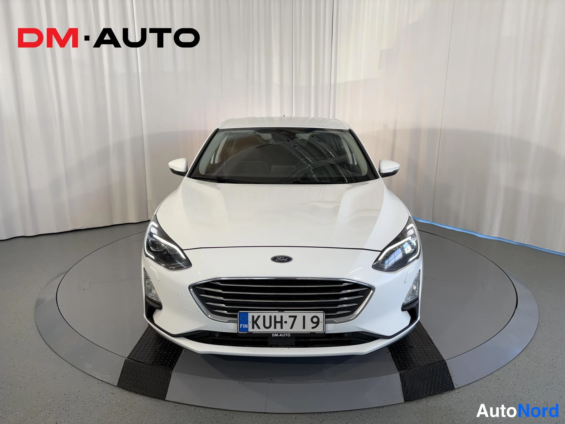 Edestä: Valkoinen Ford Focus -henkilöauto suoraan edestä, Ford-merkki konepellissä ja rekisterikilpi.