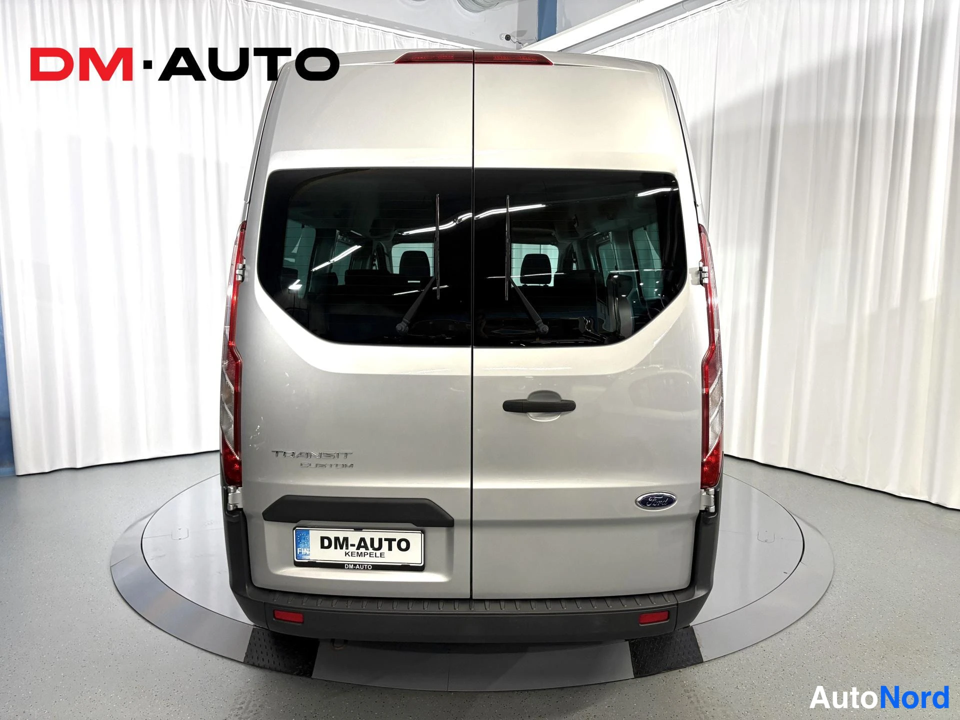 Takaa: Ford Transit Customin takaosa suoraan takaa; takaikkuna, takavaloet, takapuskuri ja rekisteritunnus DM-AUTO.