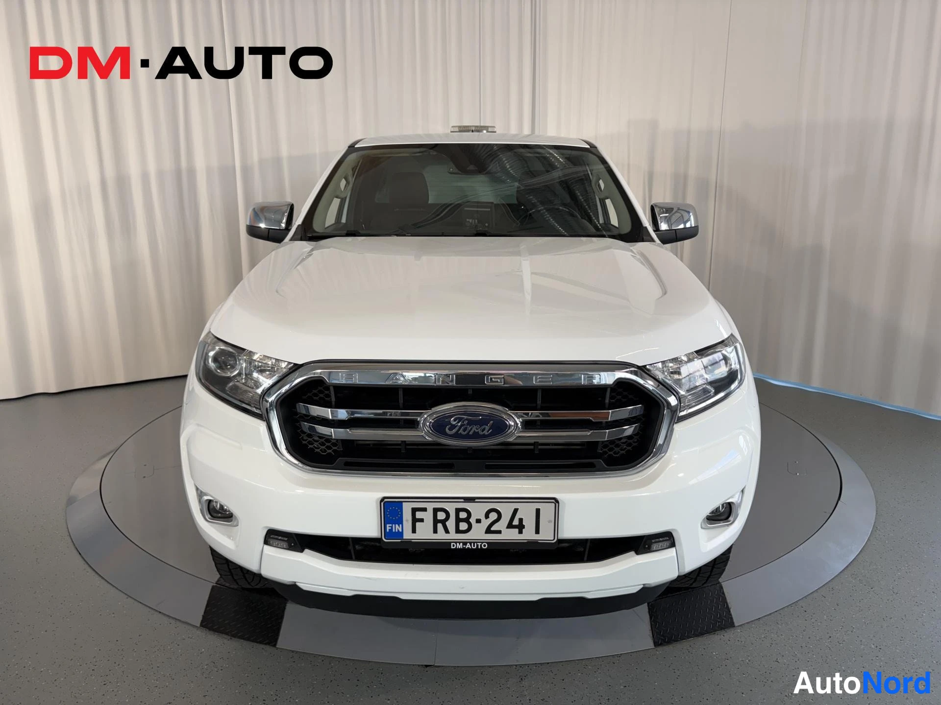 Edestä: Valkoinen Ford Ranger suoraan edestä, kromisäleiköllä ja NIL-alueella oleva rekisterikilpi.