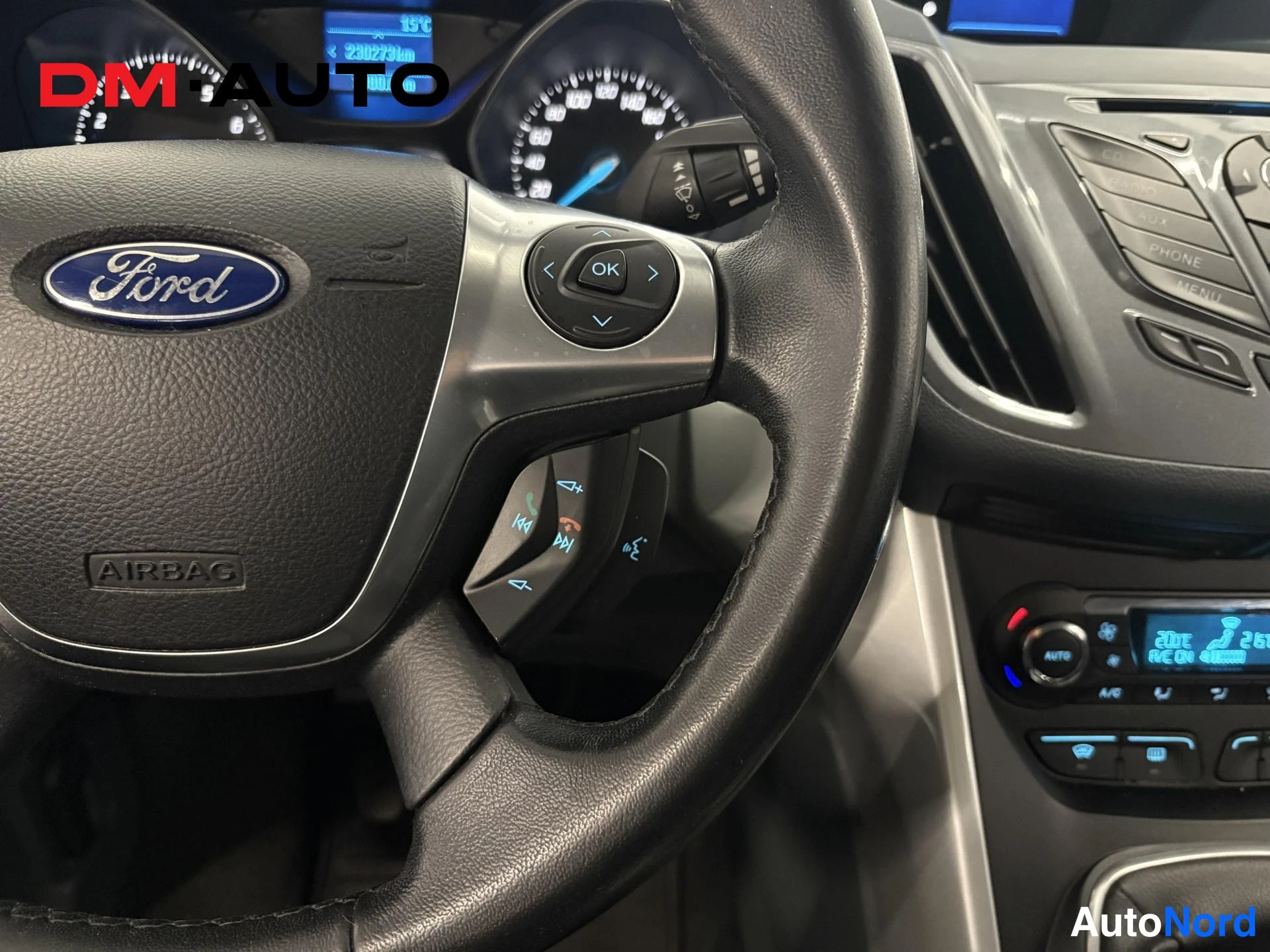 Muu: Ohjauspyörän Ford-tunnuksen lähikuva, mittaristo ja automaattisen ilmastoinnin paneeli näkyvät taustalla.