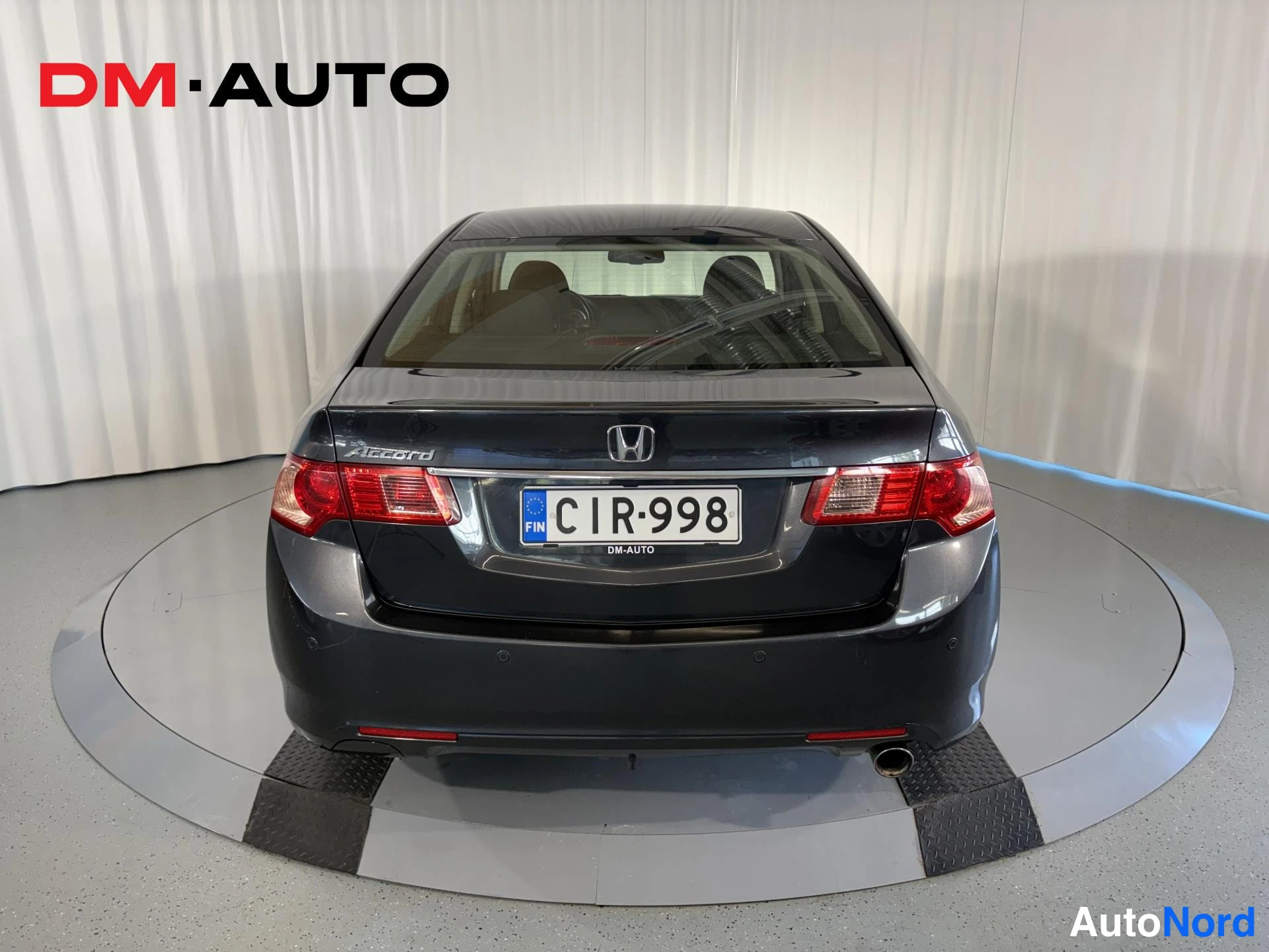 Takaa: Takaapäin kuvattu tummanharmaa Honda Accord -sedan, jossa näkyvät taka­valot, Accord-merkintä ja rekisteritunnus.