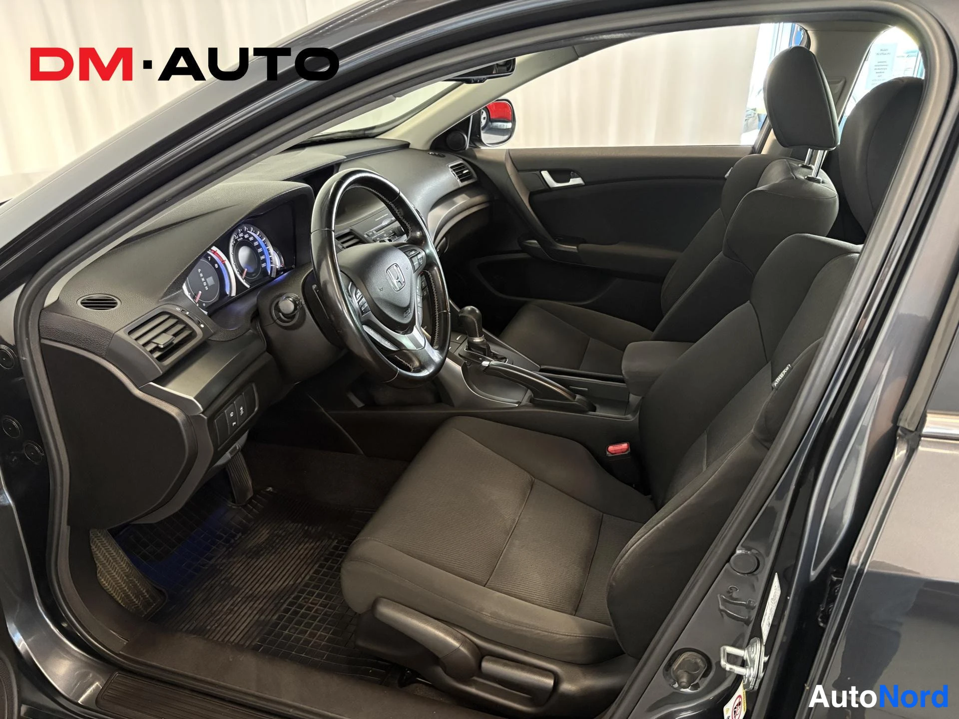 Muu: Honda Accordin matkustamo avoimesti etuovesta katsottuna: tumma sisusta, kuljettajan penkki ja kojelauta nakyyvat.