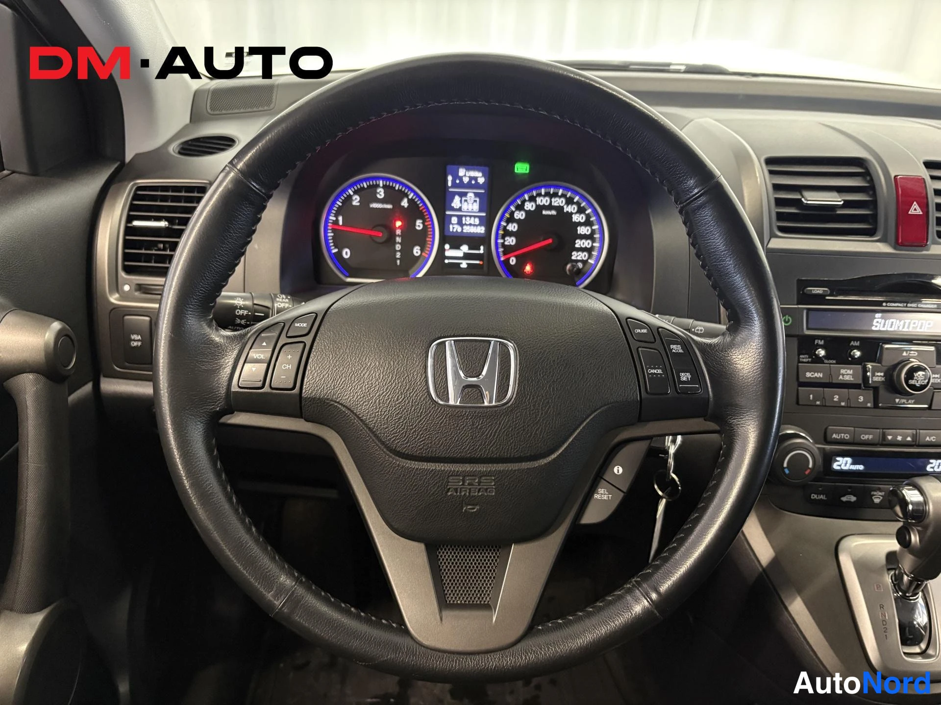 Muu: Lähikuva Honda CR-V:n ohjauspyörästä ja mittaristosta; näytössä kokonaislukemat 0 km ja 1049 km, sekä SuomiPop-radiopaneeli keskirivi- ja AUTO/AC-painikkeineen.