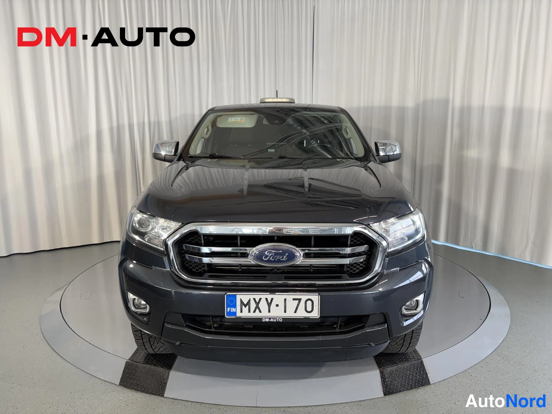 Edestä: Tummanharmaa Ford Ranger suoraan edestä: konepelti, etulasinpyyhkijät ja Ford-logo näkyvät, rekisterikilpi.
