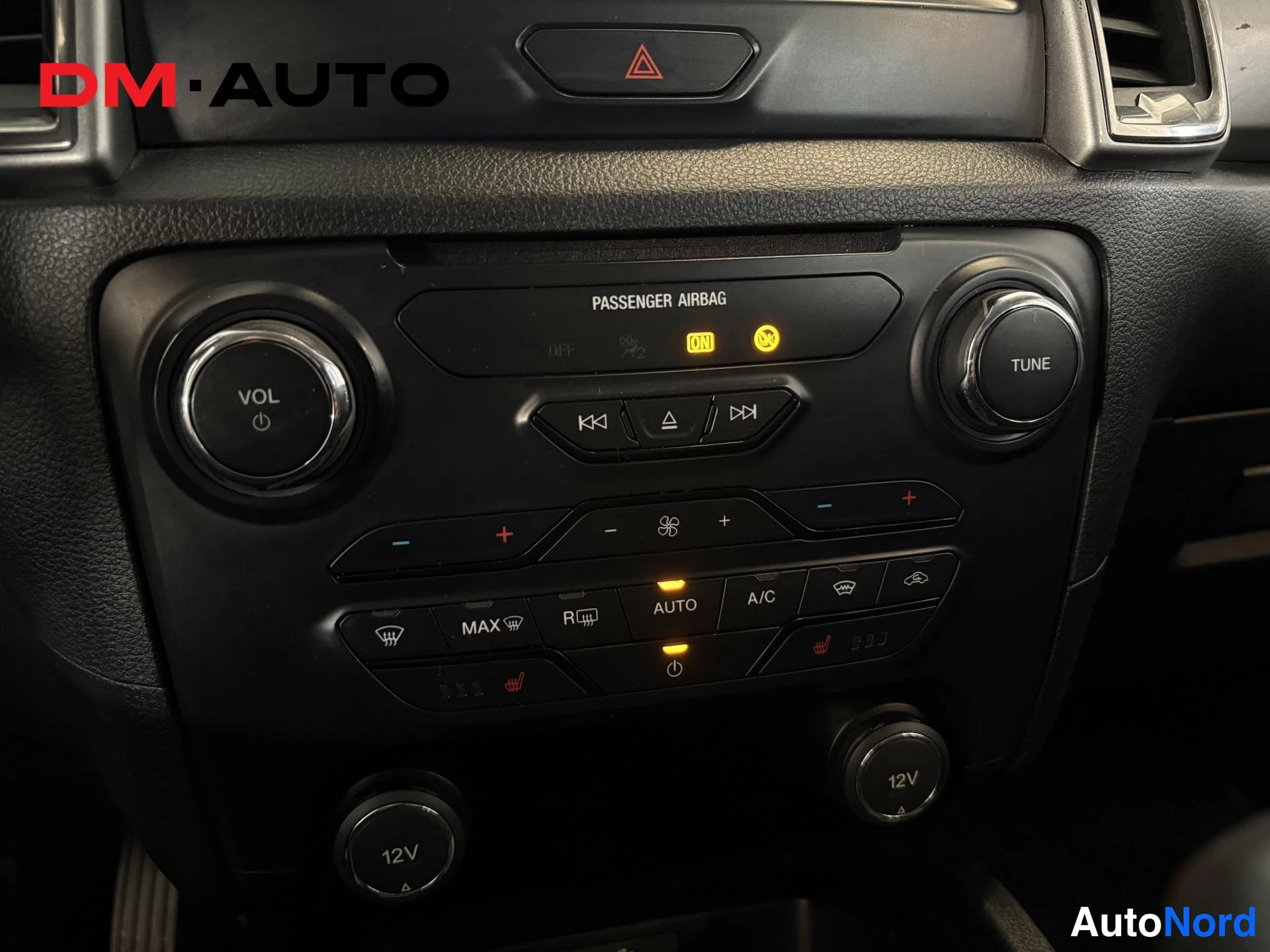 Muu: Fiat? Ford-mallin kojelaudan keskikonsoli: ilmastointipaneeli A/C- ja AUTO-napilla, äänenvoimakkuus- ja TUNE-säätimet, PASSenger AIRBAG -tilavalikko ja kaksi 12