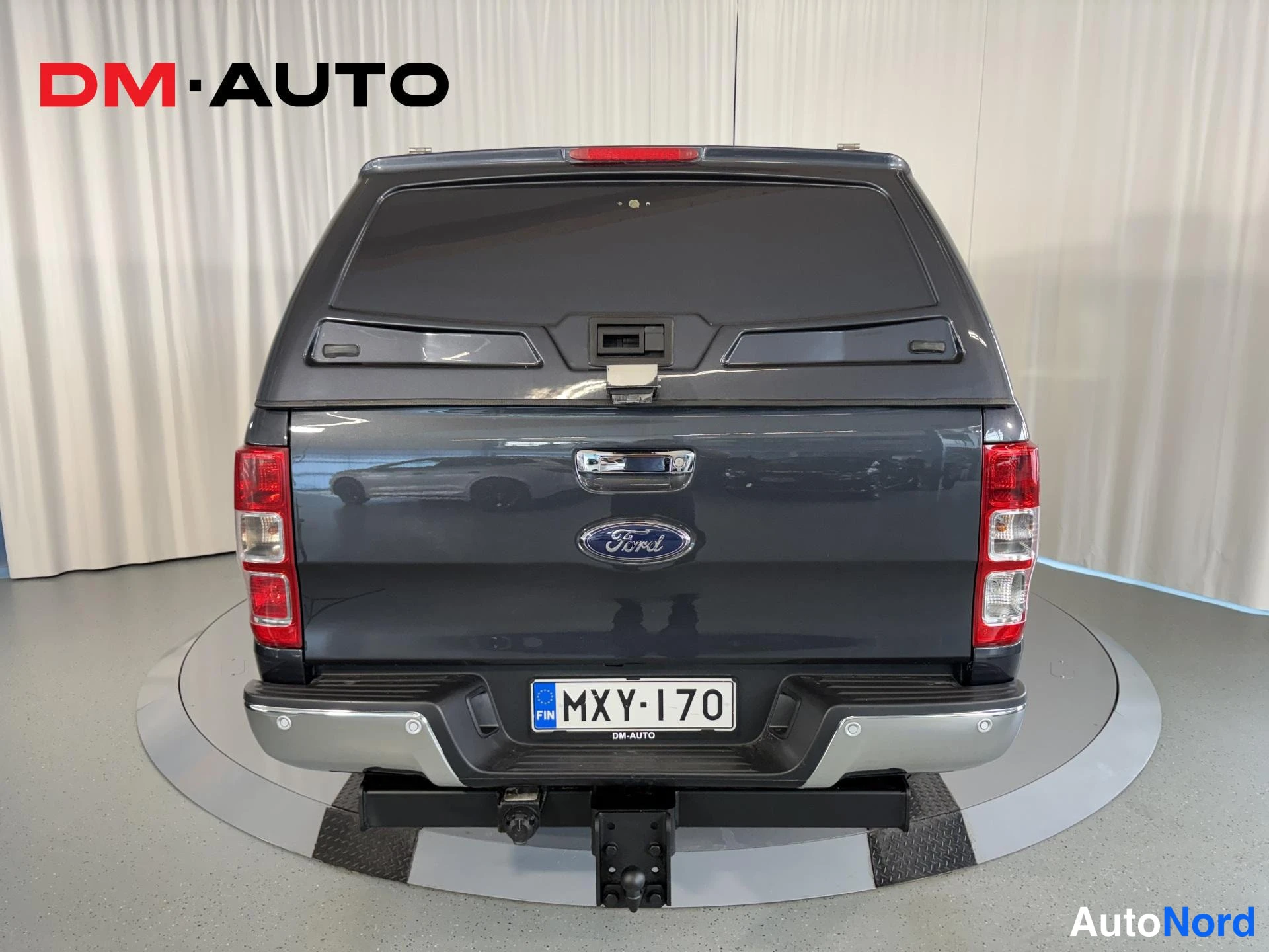 Takaa: Suora takanäkymä tummanharmaasta Ford Rangerista; Ford-merkki, takavalot, rekisterikilpi ja vedettävä vetokoukku lavakannen alla.
