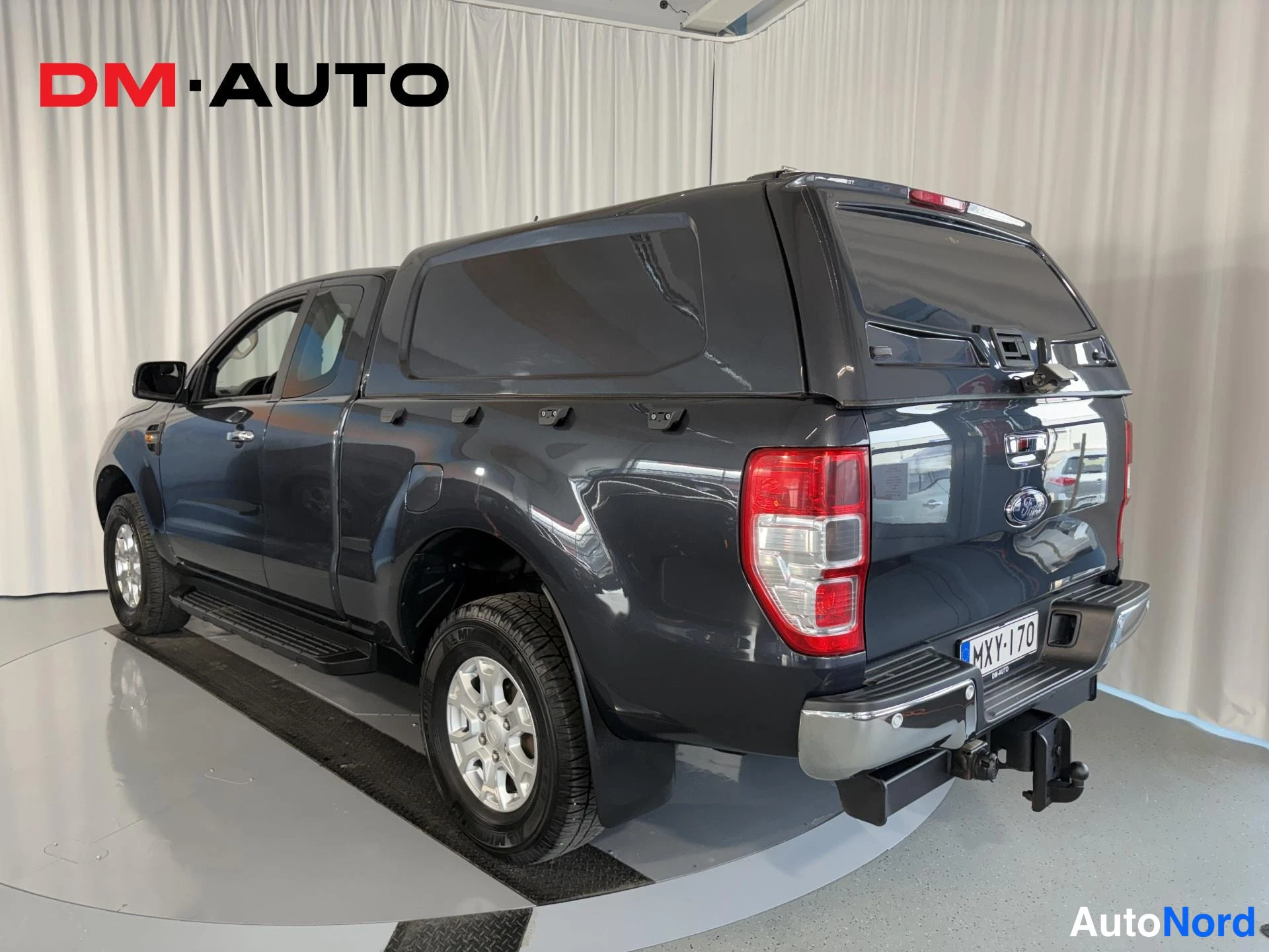 Takaviisto: Taka­kolmasosanäkymä tummanharmaasta Ford Ranger -avolavasta toisesta sivusta; takavalot, Ford-merkki, rekisterikilpi, kylkijalka ja vetokoukku näkyvät.