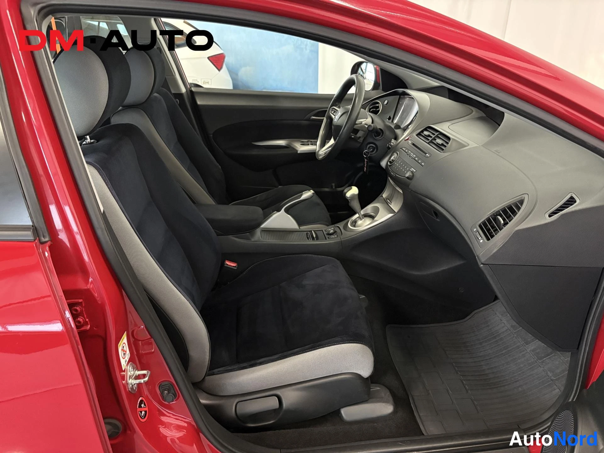 Etuviisto, nokka oikealle: Honda Civicin etuistuin ja kojelauta mustalla sisustuksella, ohjauspyörä ja vaihtajan keila näkyvät avoimesta kuljettajan ovesta.