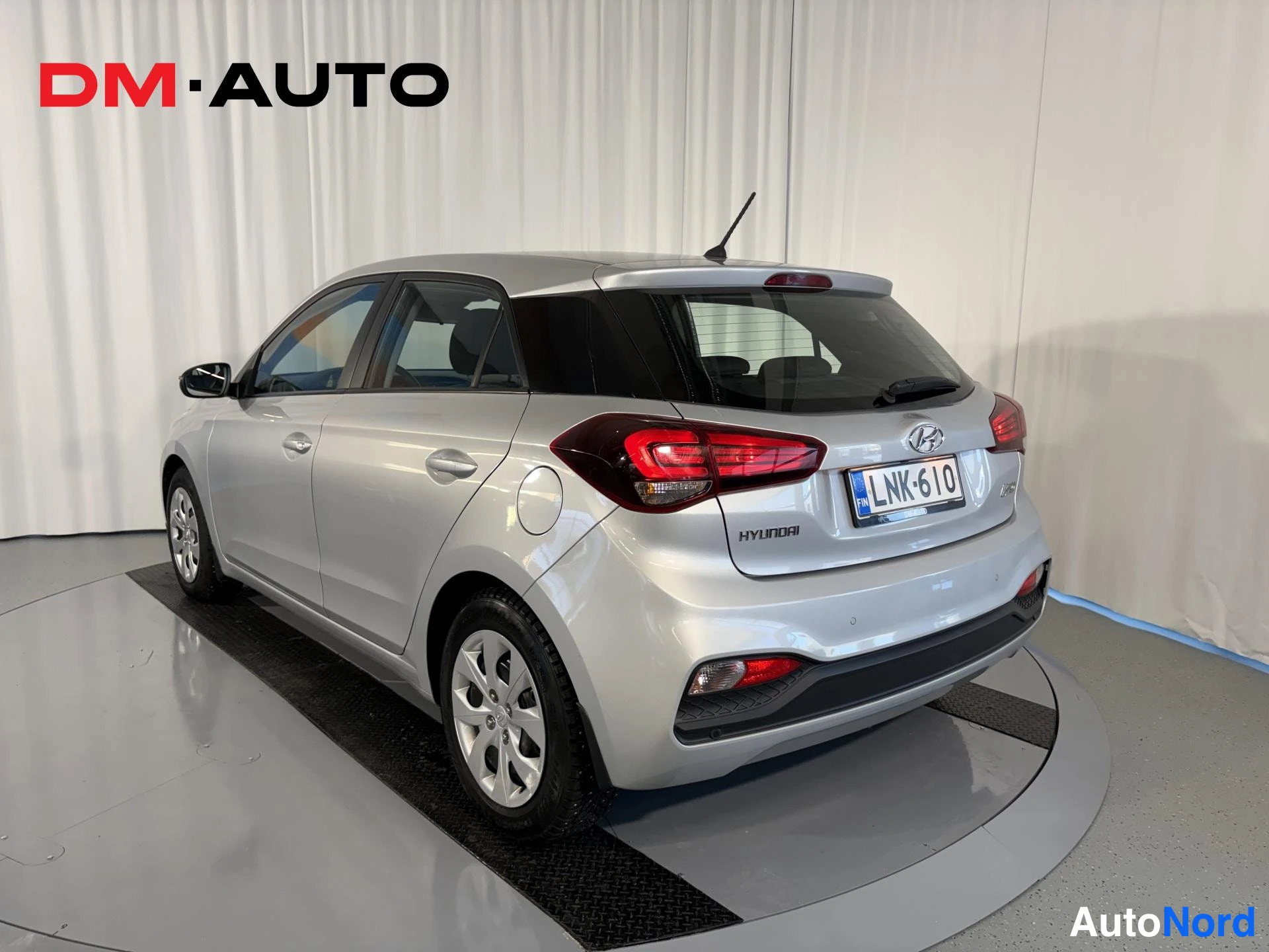 Takaviisto: Hyundai i20 -porssikuva takaa vasemmalta kulmalta; rekisterikilpi, HYUNDAI-merkintä ja hopeiset koripaneelit näkyvät.
