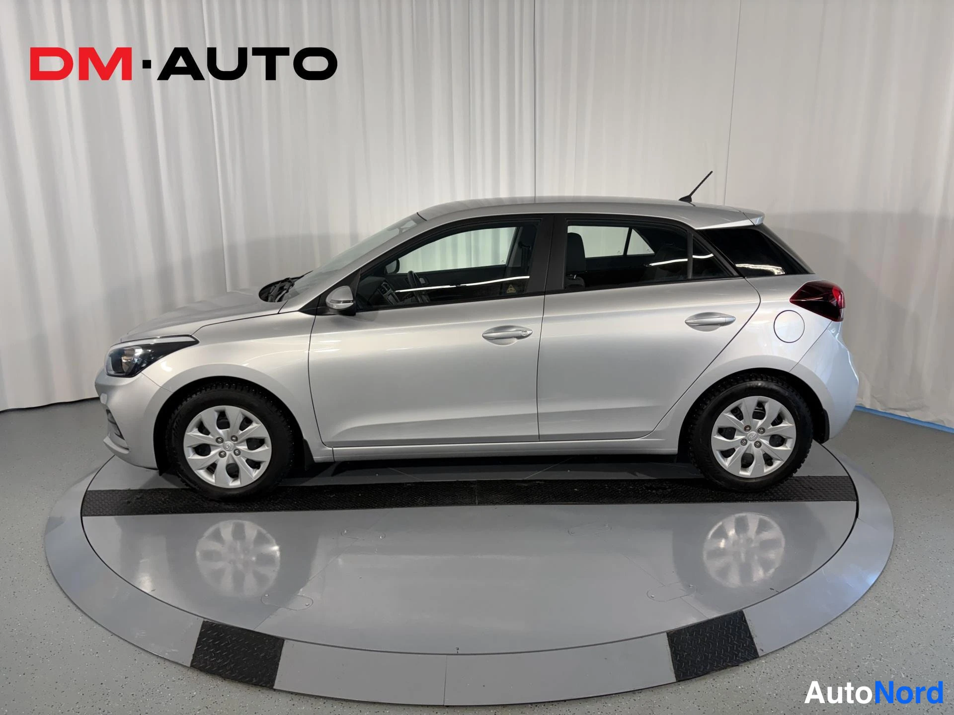 Etuviisto, nokka vasemmalle: Hyundai i20 vasemmalta sivulta; hopeiset ovet, peilit ja kolme ovea näkyvät, etuosa hieman kulmasta.