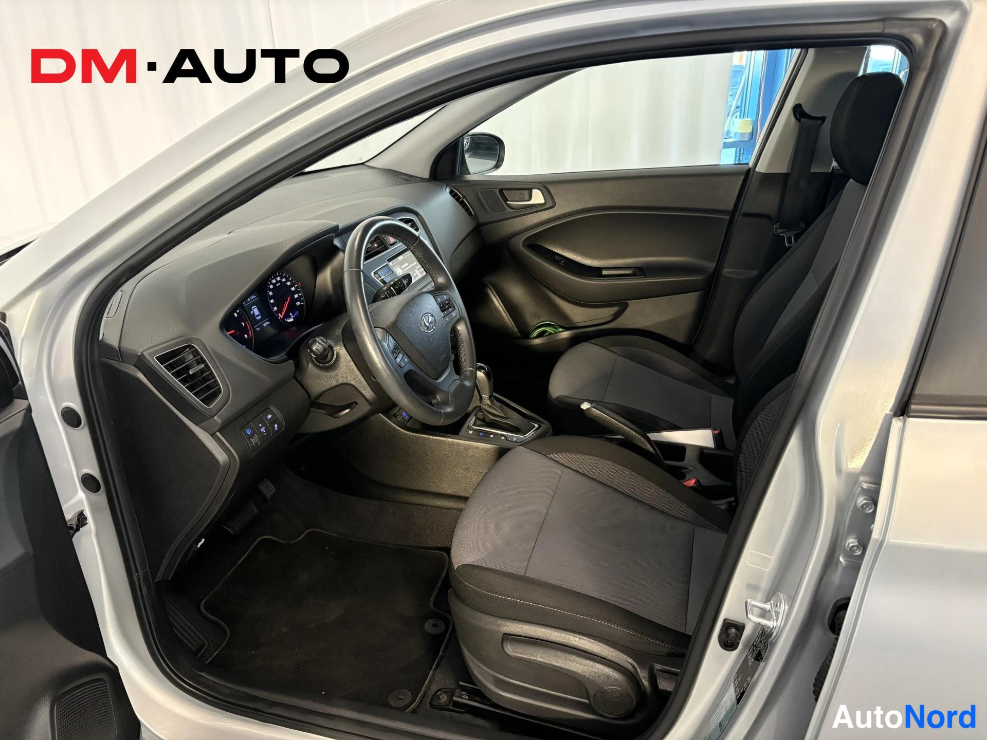 Muu: Avoin kuljettajan ovi ja etuistuin: tumma ohjaamo, kiiltävä tumma kojelauta ja Hyundai-ohjauspyörä, kankaiset istuimet.