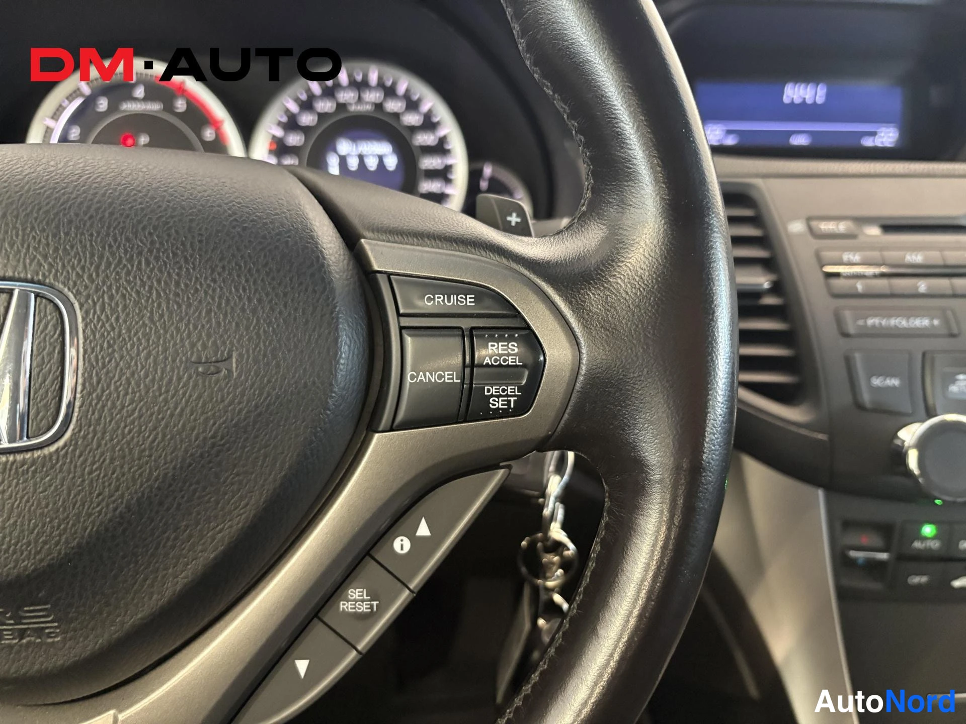 Muu: Rattipöydän lähikuva: Honda-ohjauspyörä, cruise control - ja radio-/Bluetooth-näppäimet, mittaristo ja osa keskinäytöstä taustalla.