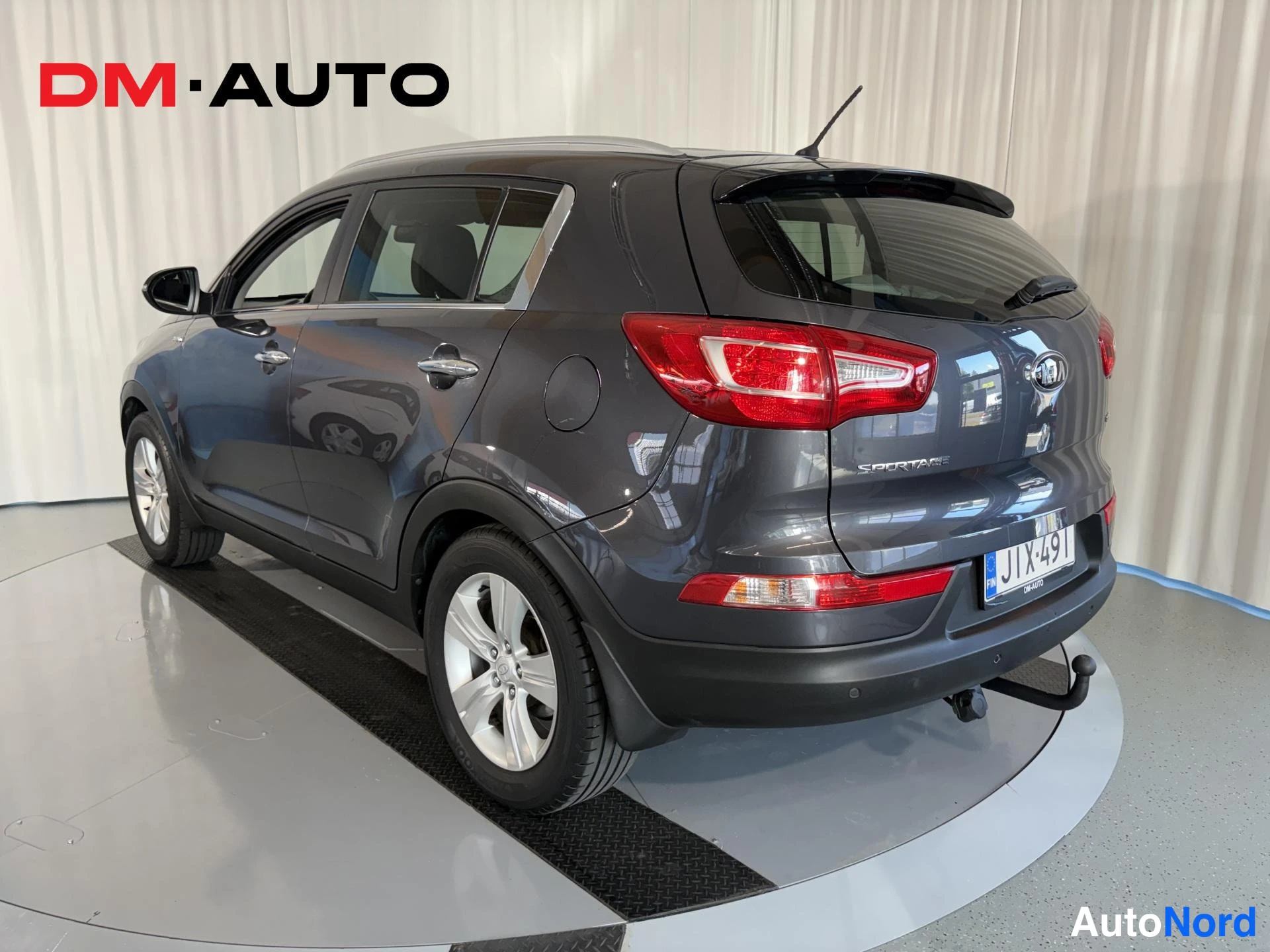 Takaviisto: Auton takaosa ja vasen sivu kolmen neljänneskulmasta: tummanharmaa Kia Sportage, hopeavanteiset pyörät, takavalot ja rekisterikilpi.