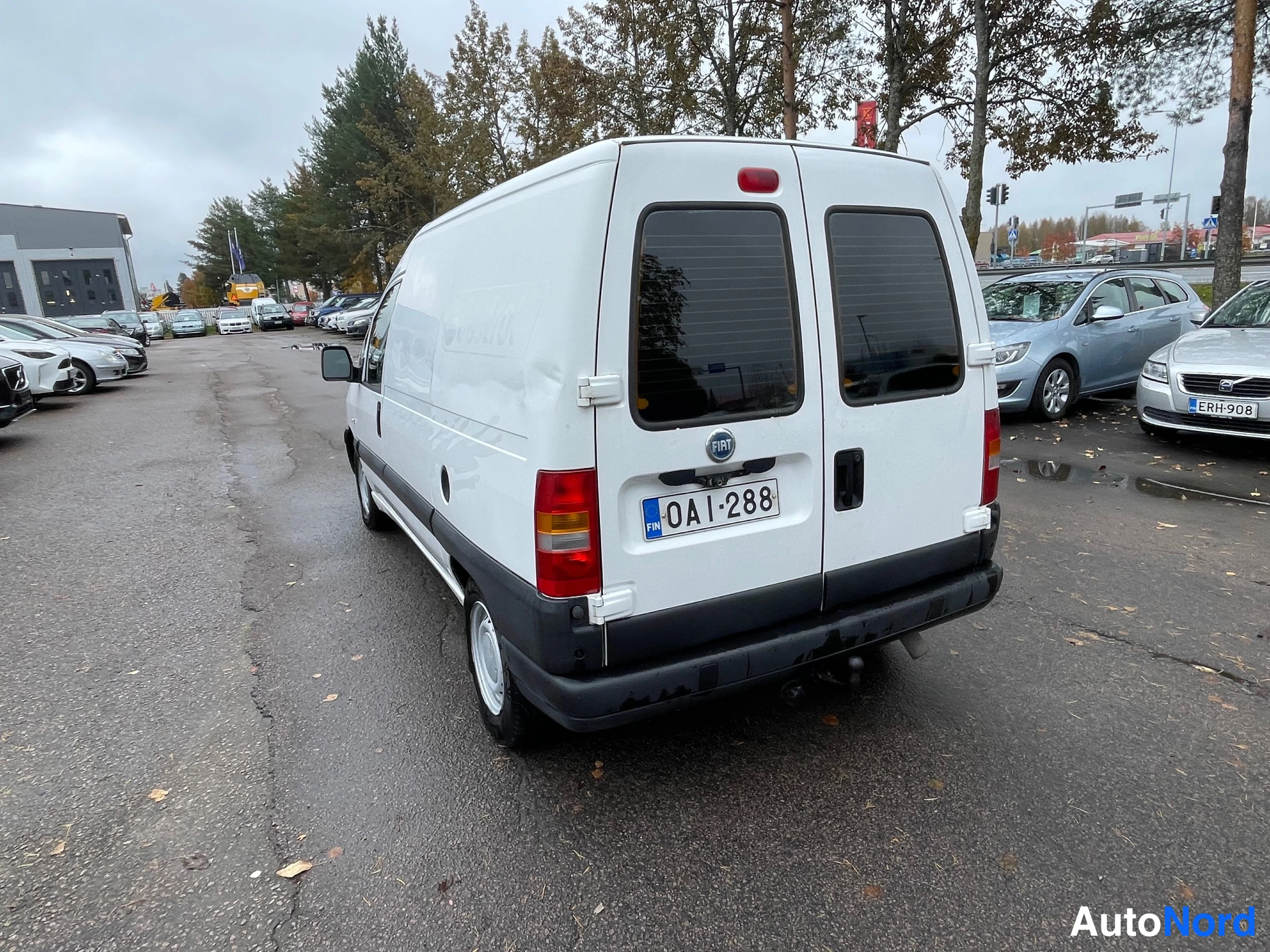 Takaviisto: Valkoisen pakettiauton takaosa ja vasen kylki takaa kuvattuna parkkipaikalla, rekisteritunnus.