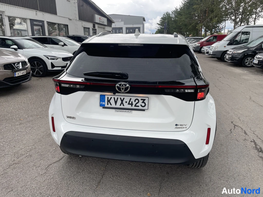 Takaa: Valkoisen Toyota Yaris Crossin peräsuora takaa, rekisterikilpi, jälkimarkkinapaikan pihalla.