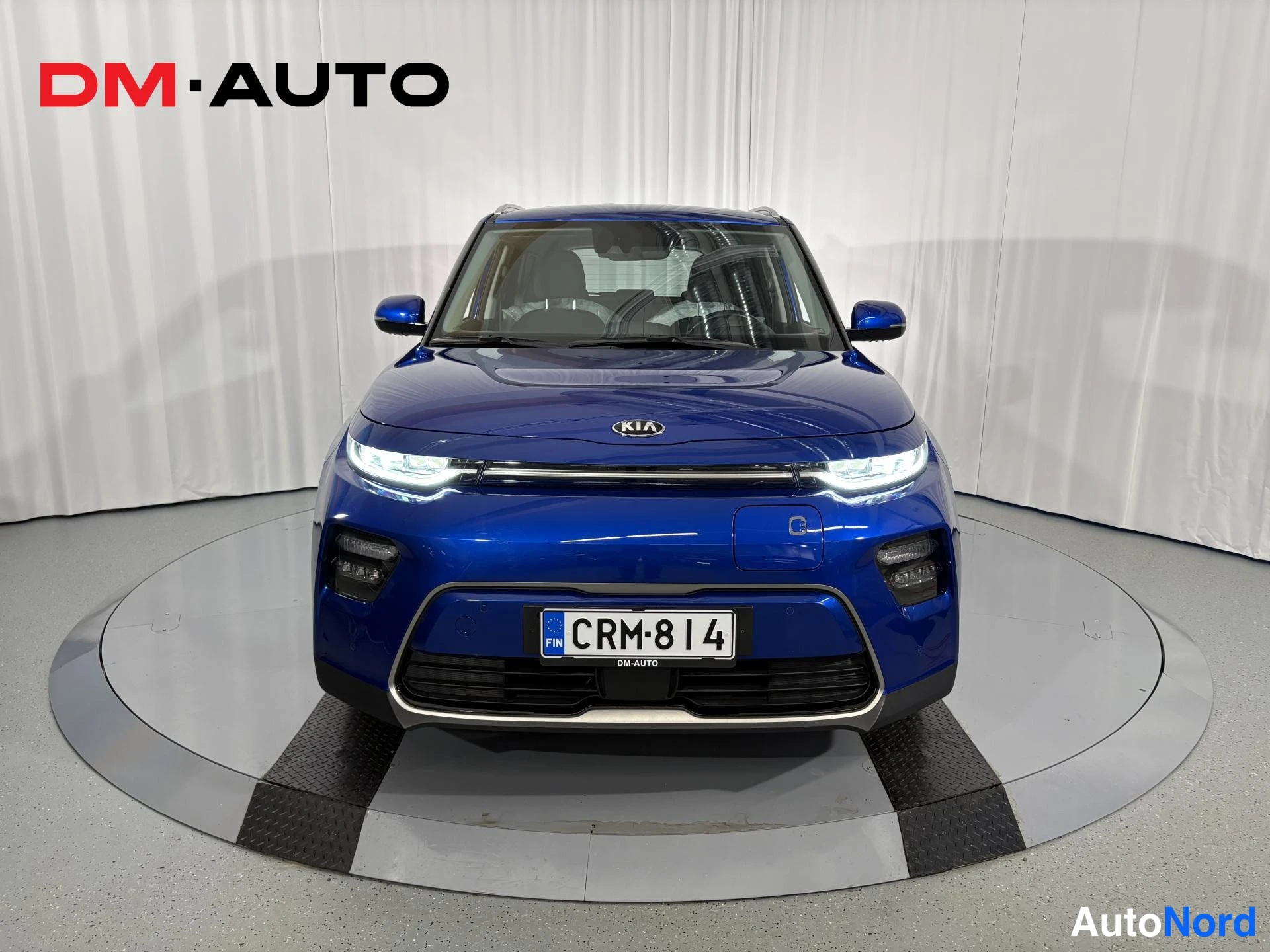 Edestä: Sininen Kia e-Soul suoraan edestäpäin, keulaa ja rekisterikilpi näkyvät valkaisualustalla.