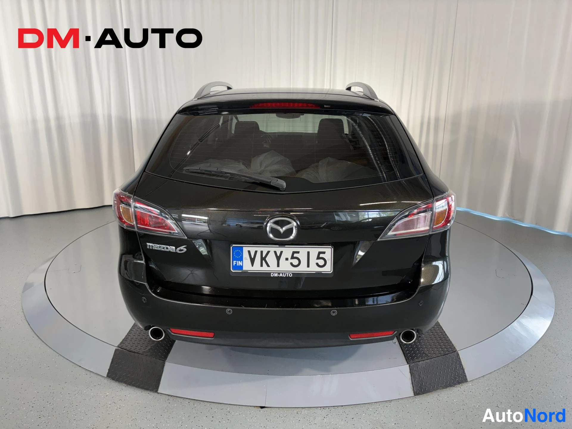 Takaa: Mustan farmariauton takaosa suoraan takaa, Mazda-merkki, takavalo ja rekisterikilpi.