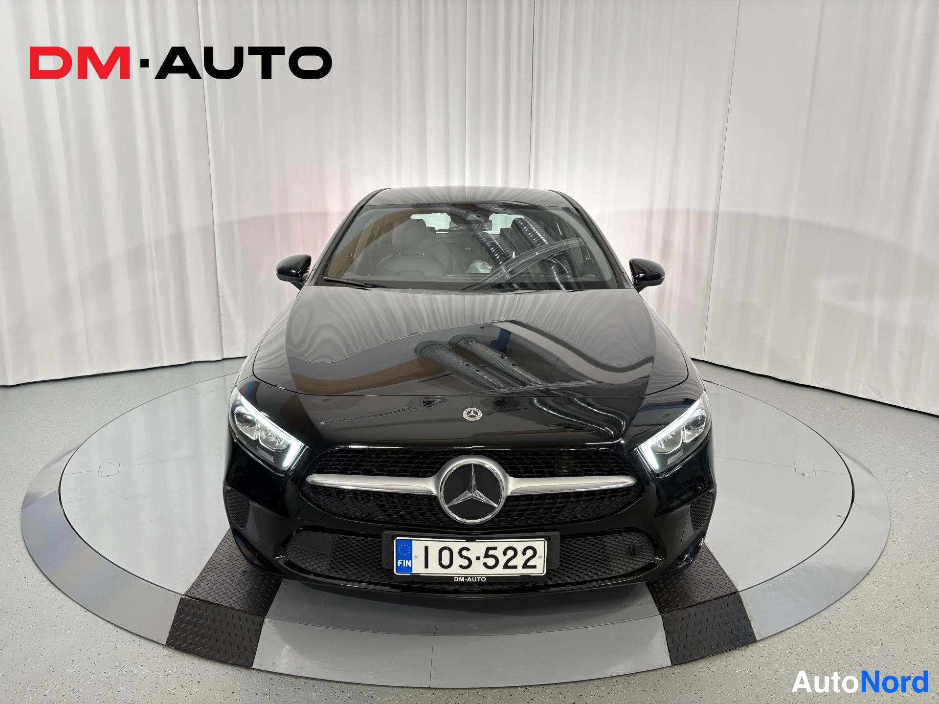 Edestä: Mustan Mercedes-Benz henkilöauton etupää suoraan edestä; etusäleikkö Mercedes-tähdellä, LED-etuvalot ja rekisterikilpi 1OS-522.