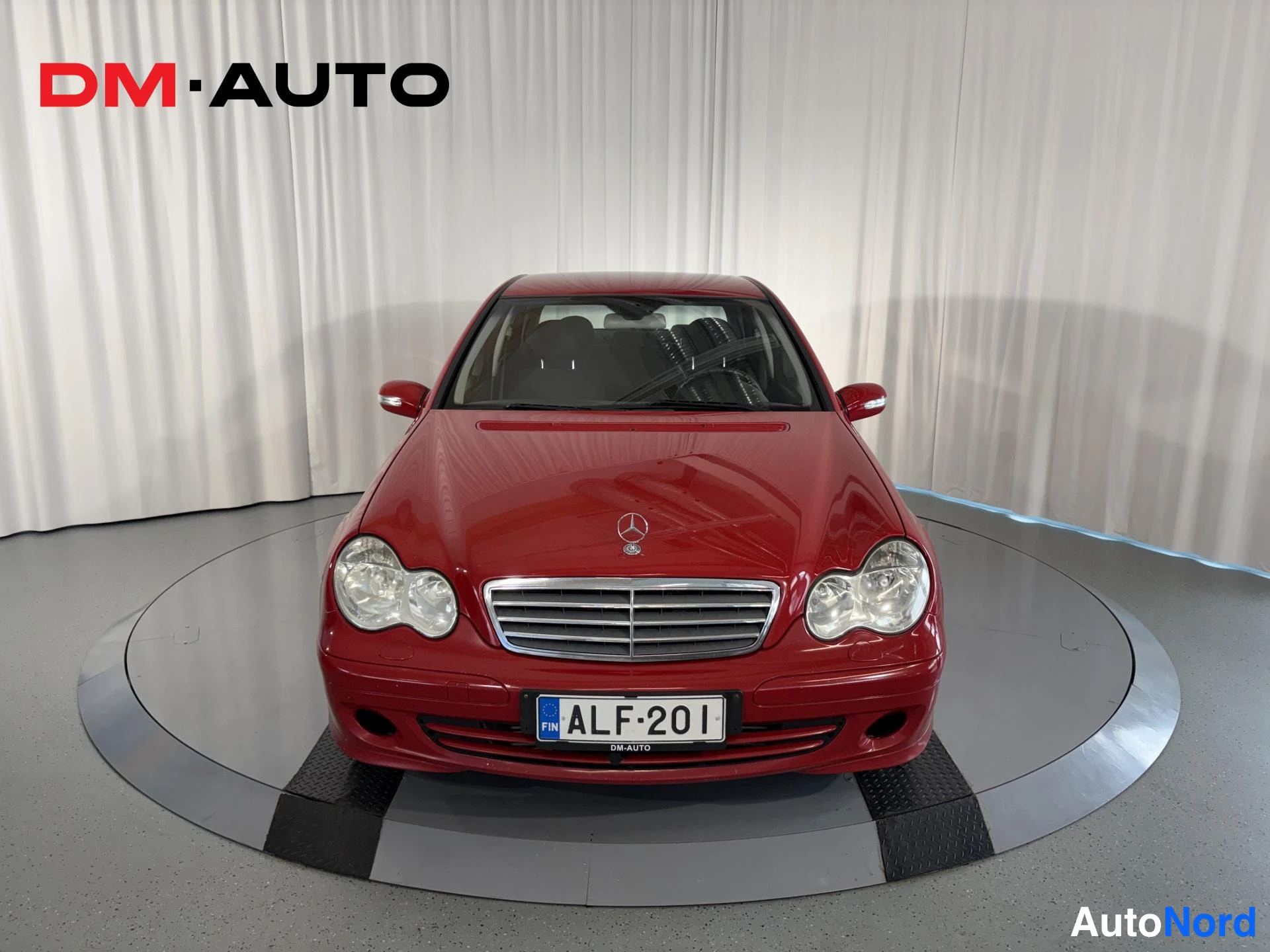 Edestä: Punainen Mercedes-Benz C-sarjan sedan suoraan edestä, etusäleikkö ja rekisterikilpi näkyvissä.