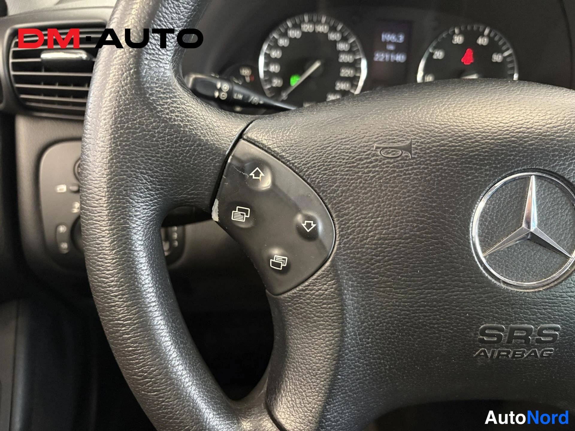 Muu: Erittäin lähikuva ohjauspyörästä: SRS AIRbag-merkintä, Mercedes-tähti ja nappien merkit; mittaristo osittain näkyvissä taustalla.