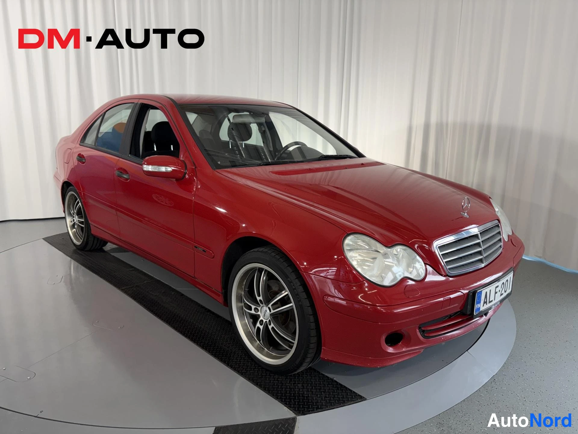 Etuviisto, nokka oikealle: Punainen Mercedes-Benz C-sarjan sedan etuviistöstä oikealta, rekisterikilpi ja kevytmetallivanteet näkyvissä.