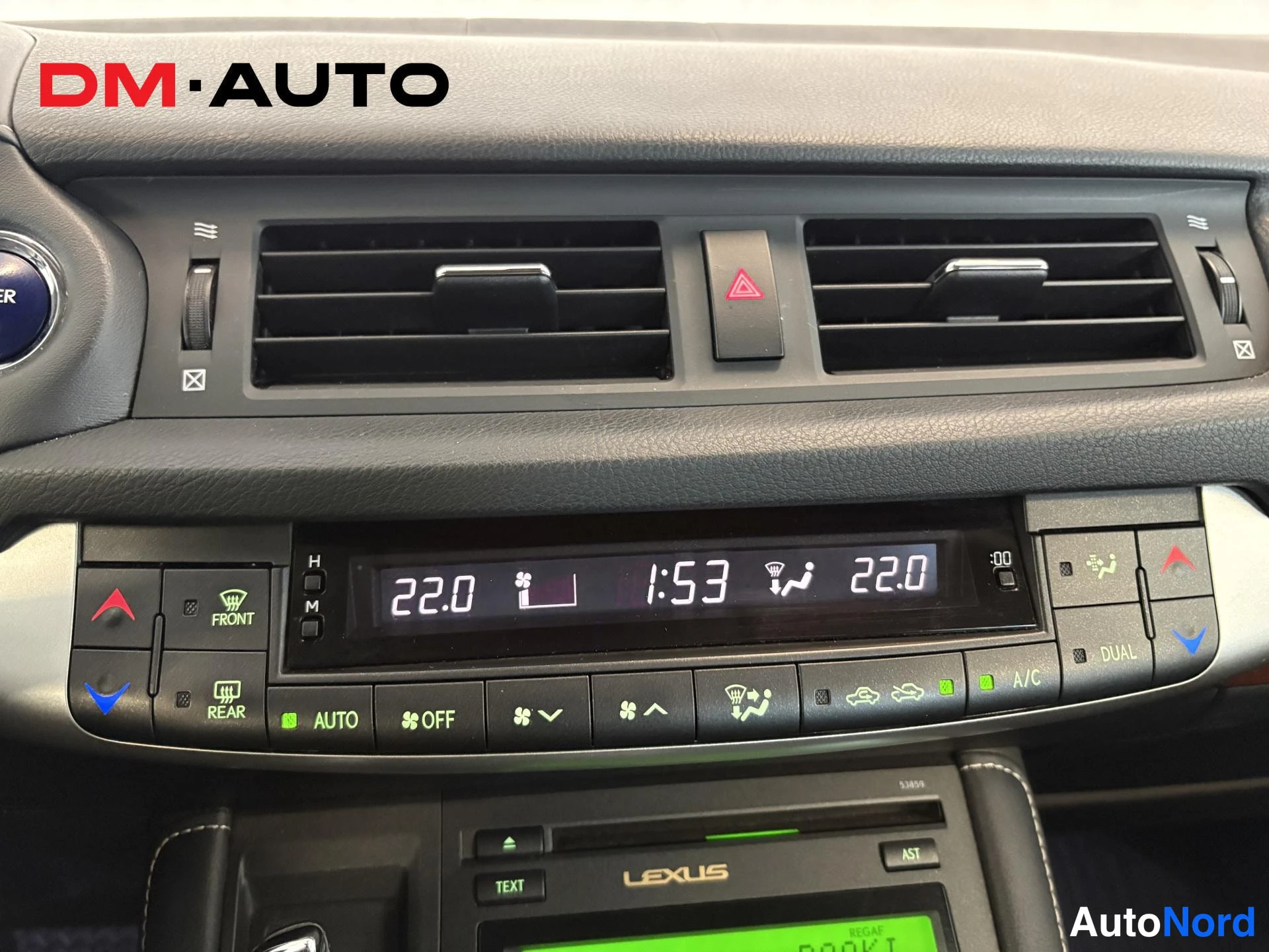 Muu: Kojelaudan ilmastointipaneelin lähikuva: kaksi ilmanvaihtoluukkua, varoitusnappi, näytöllä 22.0 ja 22.0 sekä kello 1:53, AUTO-, OFF-, A/C- ja DUAL-painikkeet, F