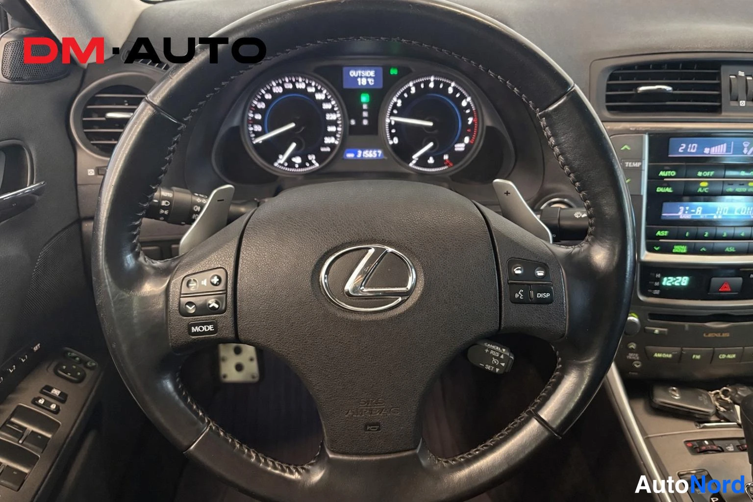 Muu: Lahikuva Lexus-ohjauspyorasta ja kojelaudan mittareista; pyorassa nappaimia ja automaatinvaihteen lapset, keskkonsolissa naytto.