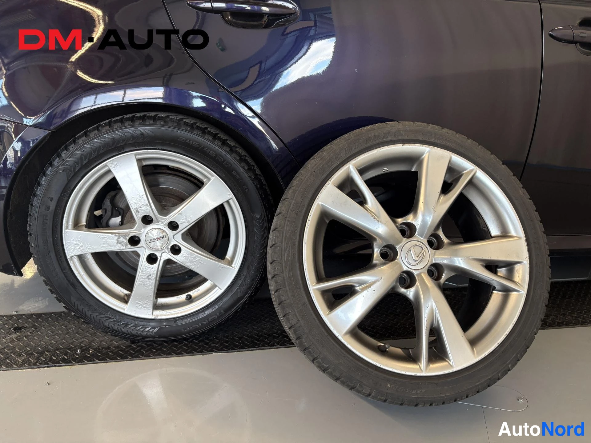 Sivulta: Lexus-auton takapyörä ja vieressä irtonainen hopeavanteellinen rengas, tumma koripaneeli taustalla.