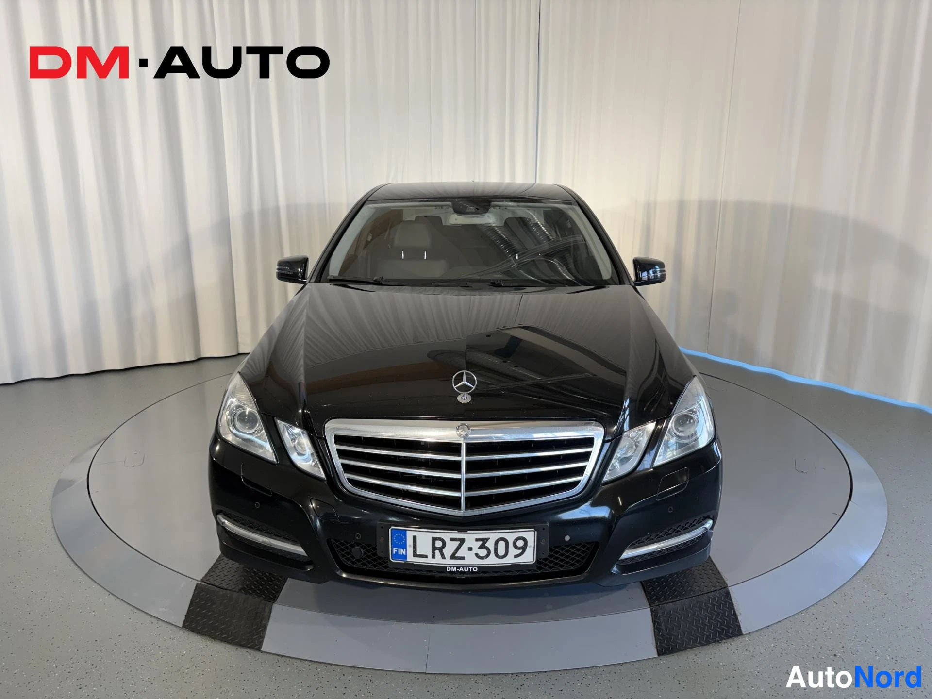 Edestä: Mustan Mercedes-Benz E-sarjan sedanin etunäkymä, rekisteri, studio-kuva pyörivällä tasolla.