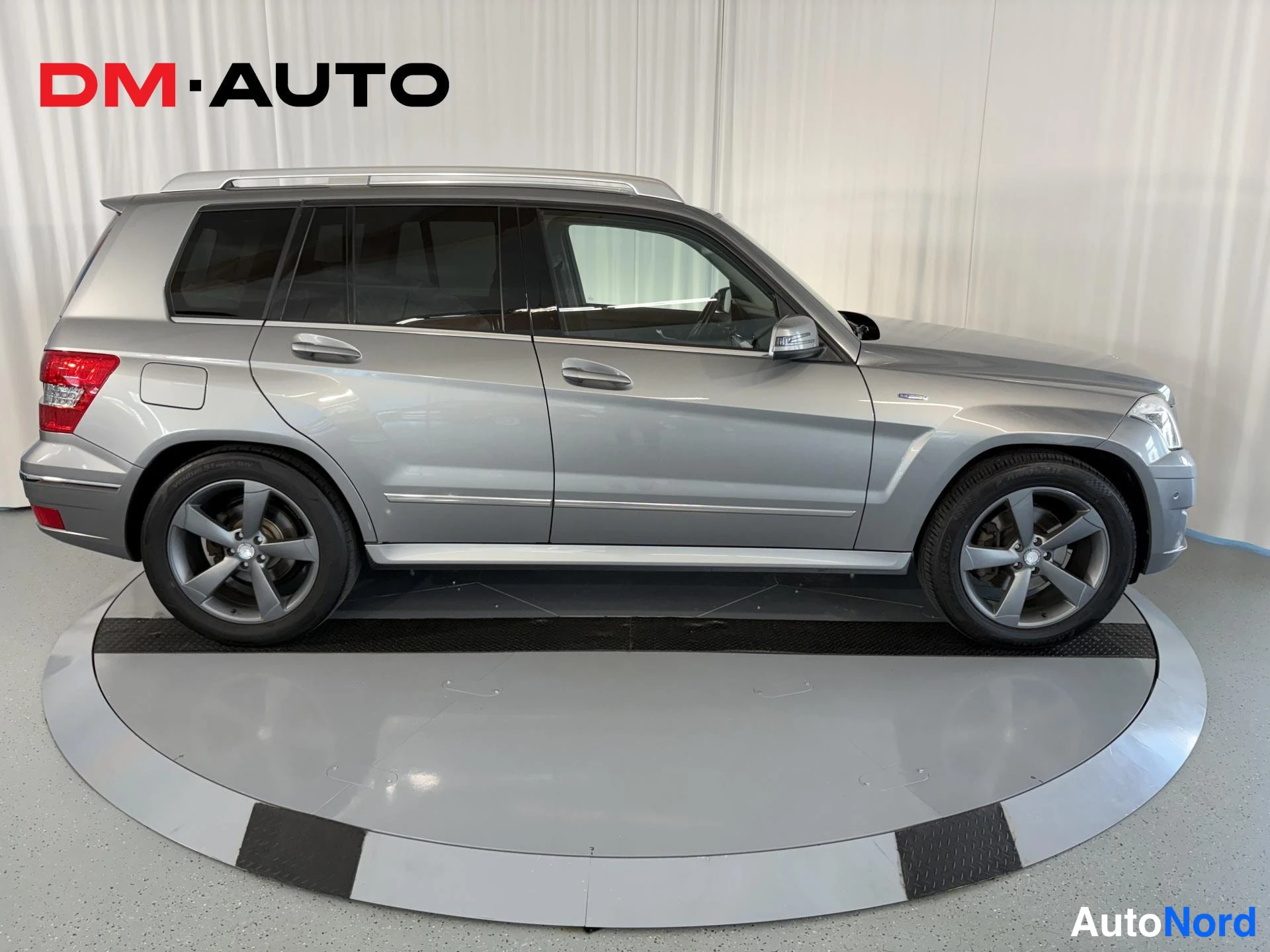 Sivulta: Hopeanharmaa Mercedes-Benz GLK:n sivunäyttö sisätiloissa, koko kylki ja pyörät näkyvät.