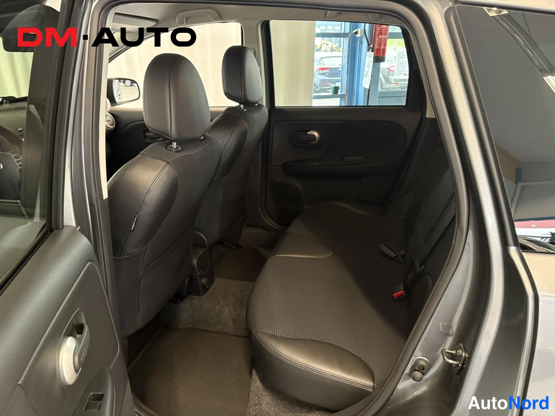 Muu: Nissan Note:n takaistuin ja avattu takiovi; mustat istuimet ja tumma ovipaneeli näkyvät sisätiloissa.