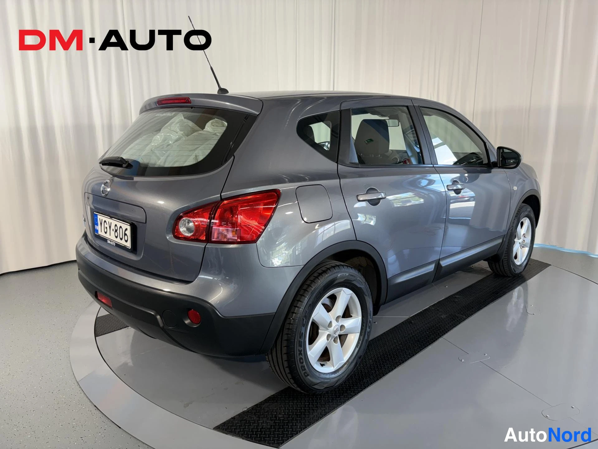 Takaviisto: Auton takaosa ja vasen sivu kolmivartalokuvassa: harmaa Nissan Qashqai, punaiset takavalot, rekisterikilpi.