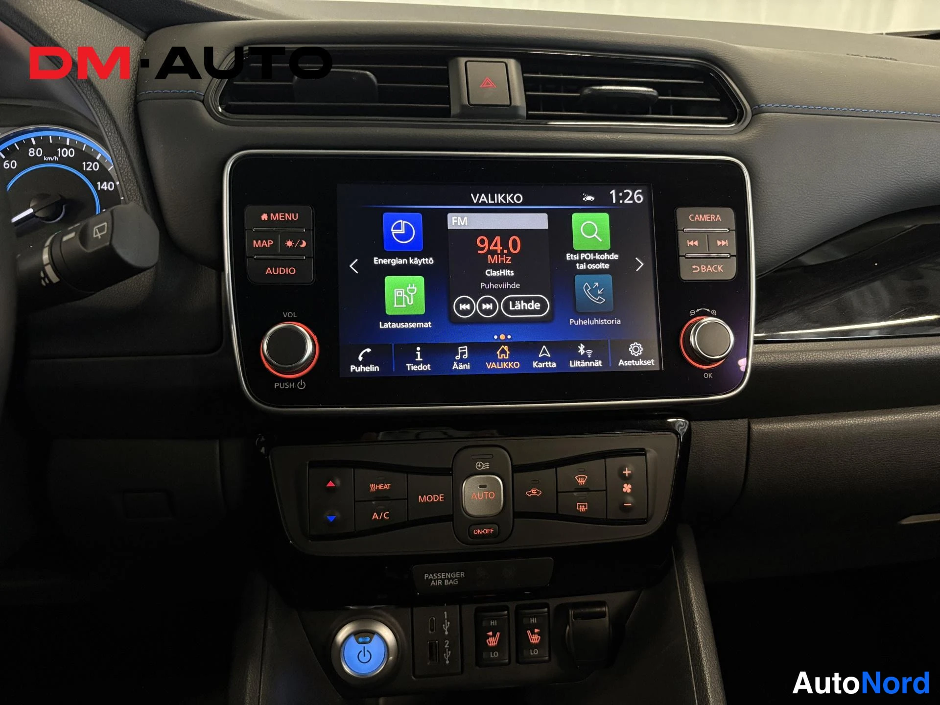 Muu: Keskikonsolin infotainment-näyttö valikossa ja automaattinen ilmastointipaneeli AUTO-painikkeella, radioasemia listassa.
