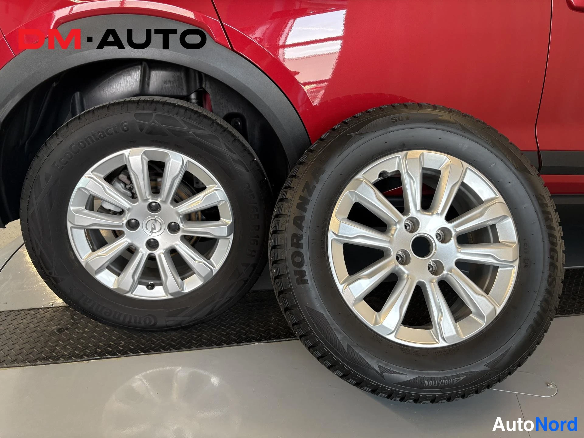 Sivulta: Lähikuva auton pyörästä ja vieressä olevasta varapyörästä; hopea vanteen pinta ja Continental- ja Bridgestone-norananz-rengaskirjoitukset näkyvät punaisen korin