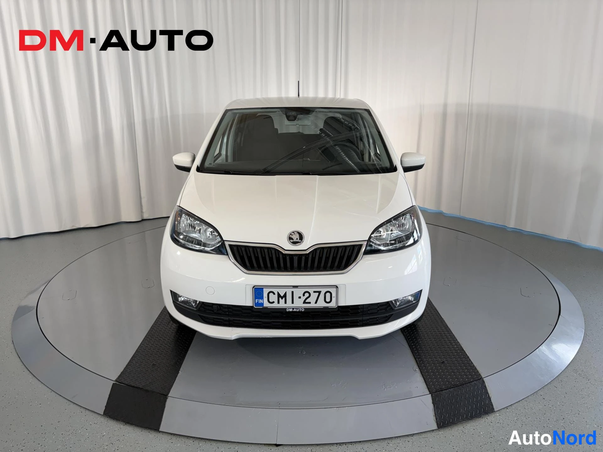 Edestä: Valkoinen Skoda Citigo suoraan edestä, etusäleikkö, ajovalot ja rekisterikilpi CM1-270 näkyvät.