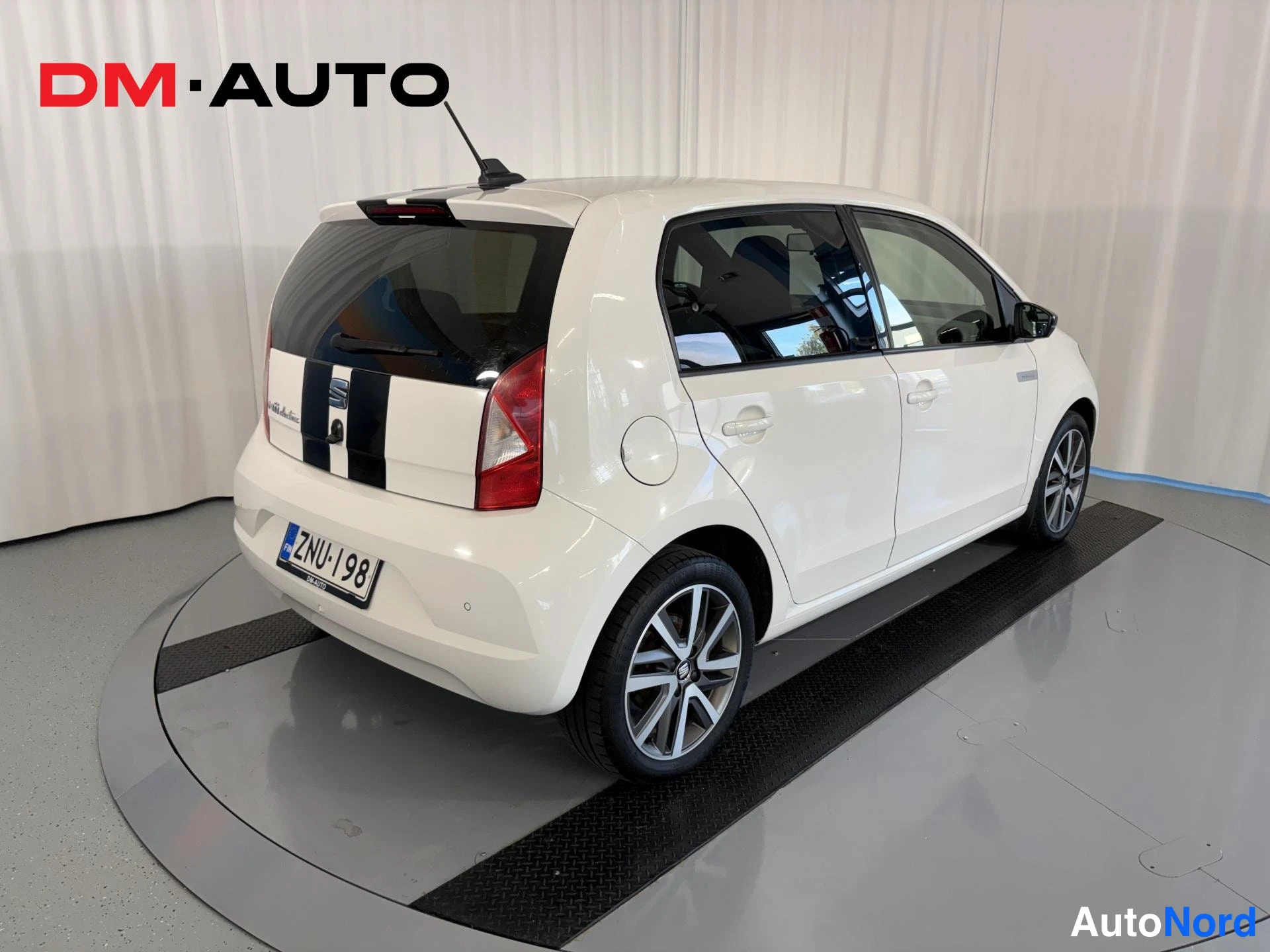 Takaviisto: Auton takakulma vasemmalta: valkoinen Seat Mii Electric, mustat kilpajuoksuraidat takaosassa, rekisteritunnus.