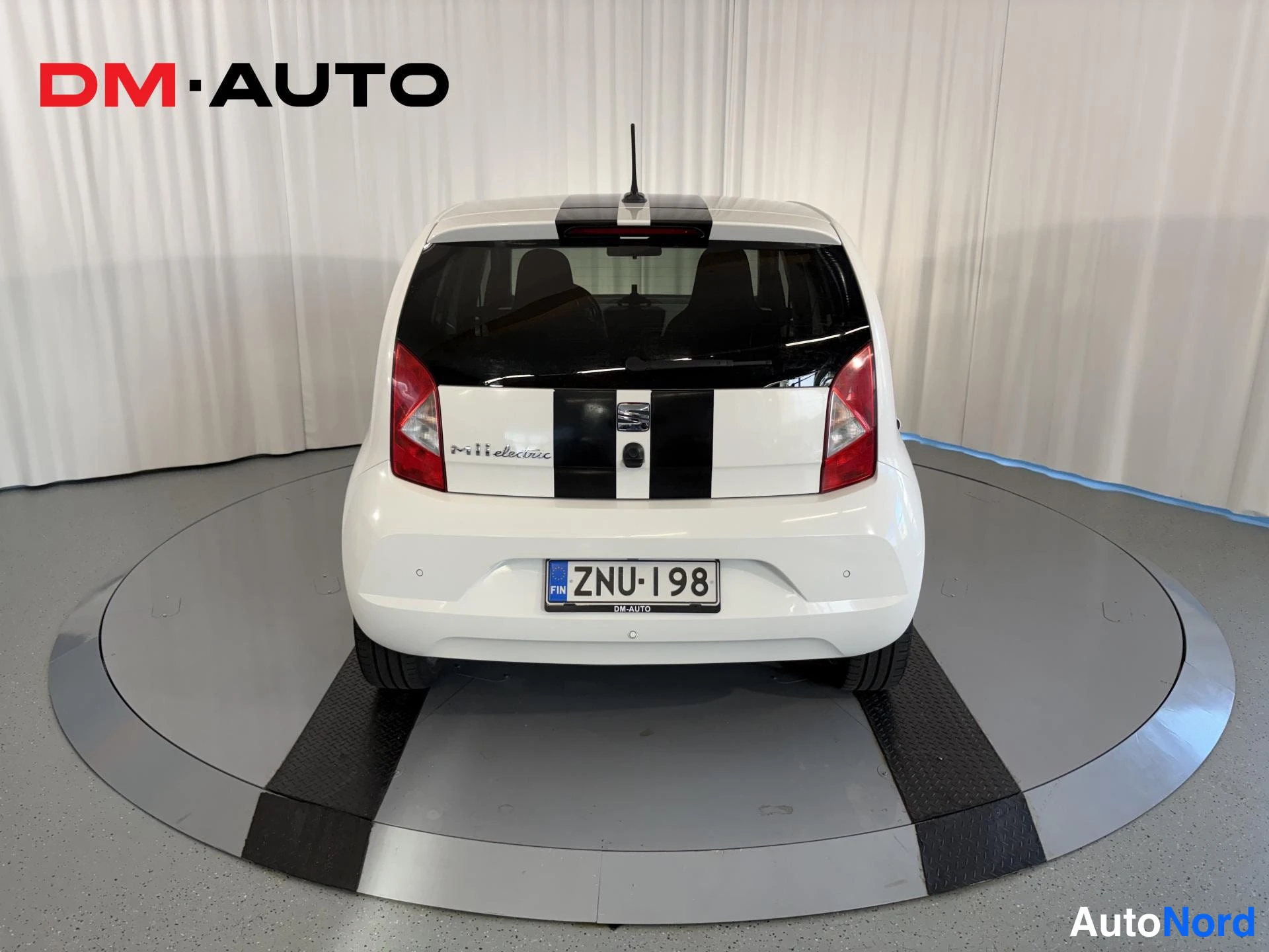 Takaa: Auton takaosa suoraan takaa: valkoinen Seat Mii Electric, musta kilparaita, rekisteritunnus.