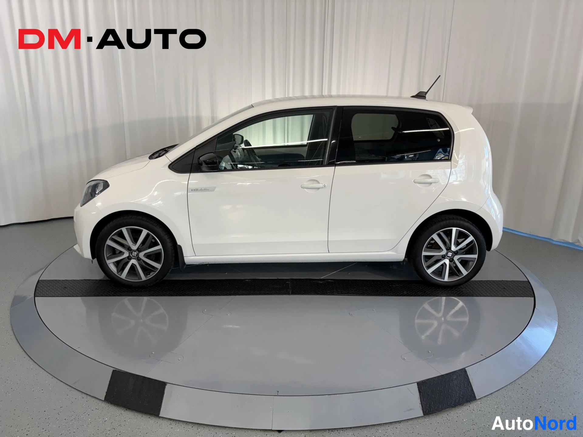 Sivulta: Auton kylki sivusta: valkoinen Seat Mii Electric, viisiovinen, mustat kattopalkit ja tummat ikkunat.