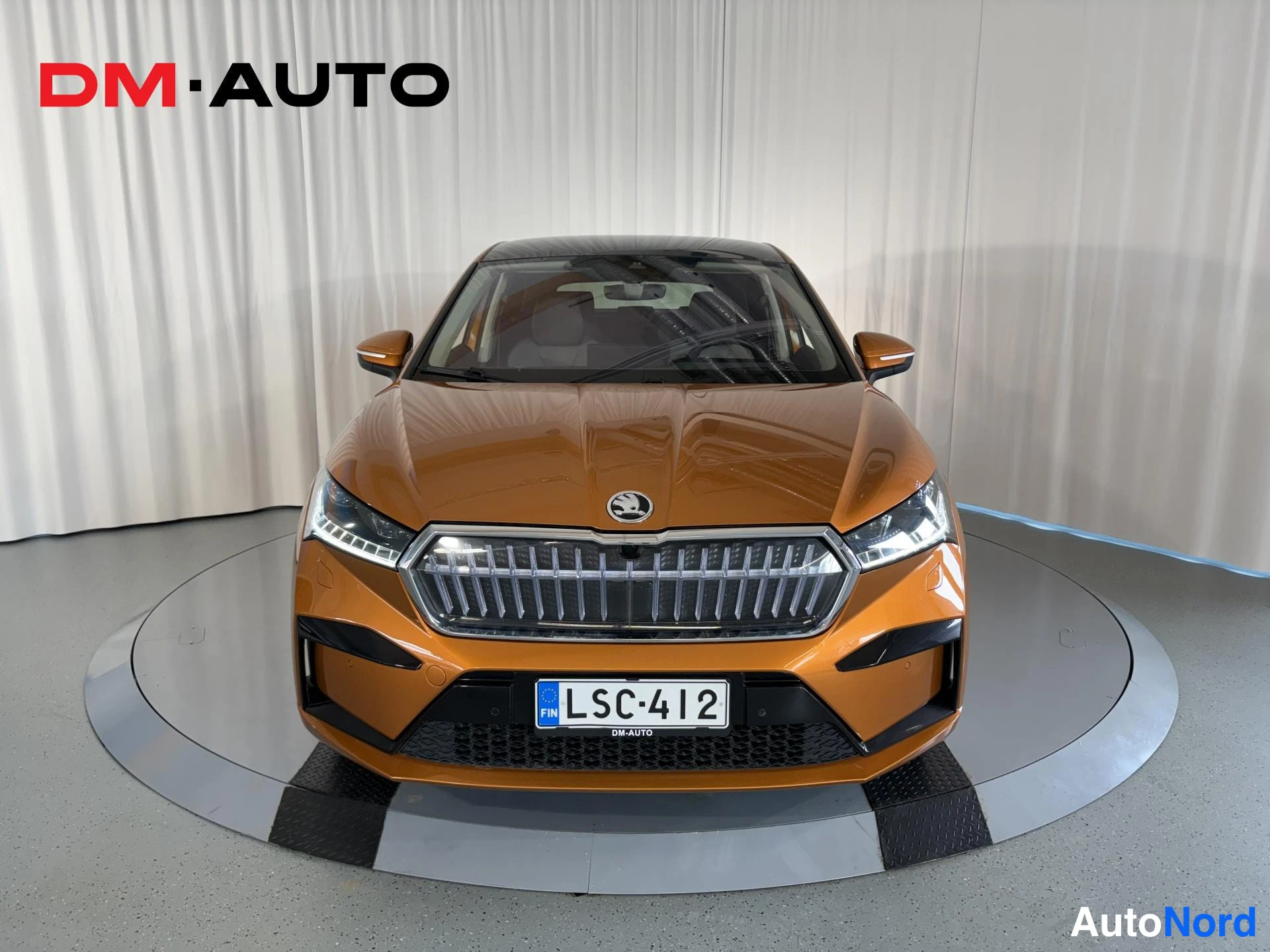 Edestä: Oranssi Skoda Enyaq Coupé suoraan edestä nähtynä, Maski-keulailme ja rekisteri.