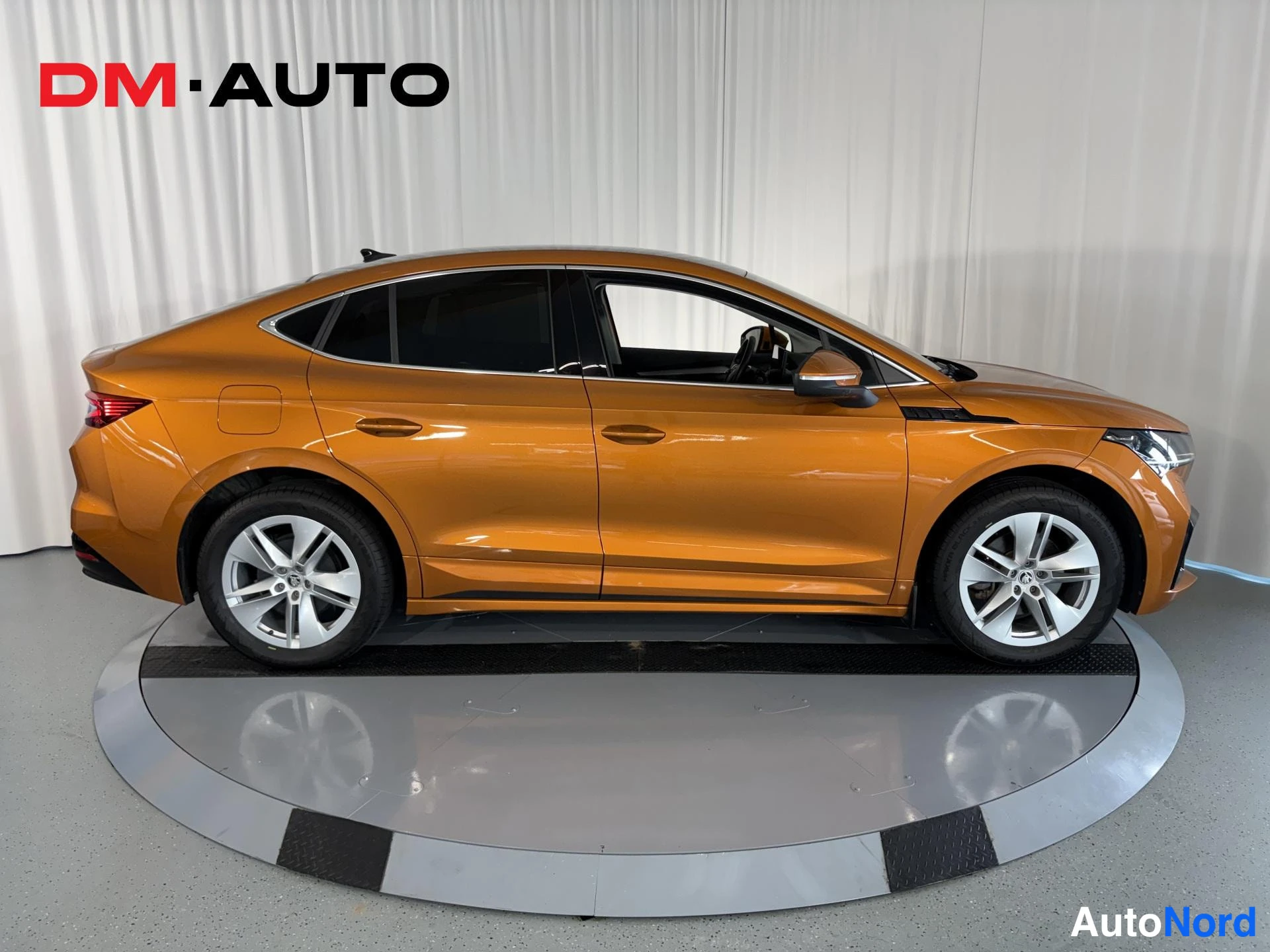 Sivulta: Oranssi Skoda Enyaq Coupé sivulta nähtynä, hopeavanteet ja tummat ikkunat.
