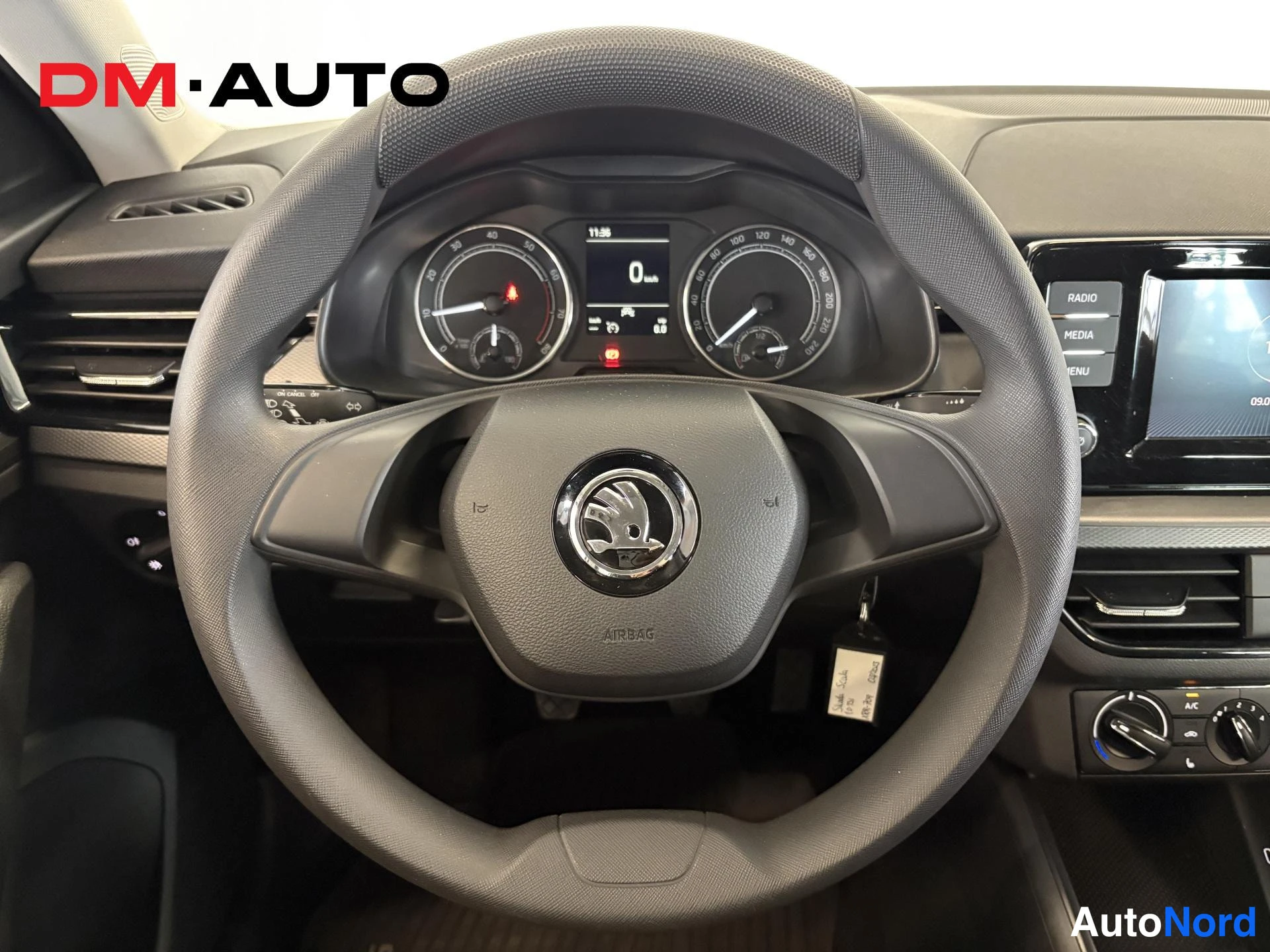 Muu: Lähikuva ohjauspyörästä ja mittaristosta: Skoda-tunnus ohjauspyörässä, AIRBAG-teksti, nopeusmittari 0 km, ja radio/MEDIA/MENU-napit oikealla.