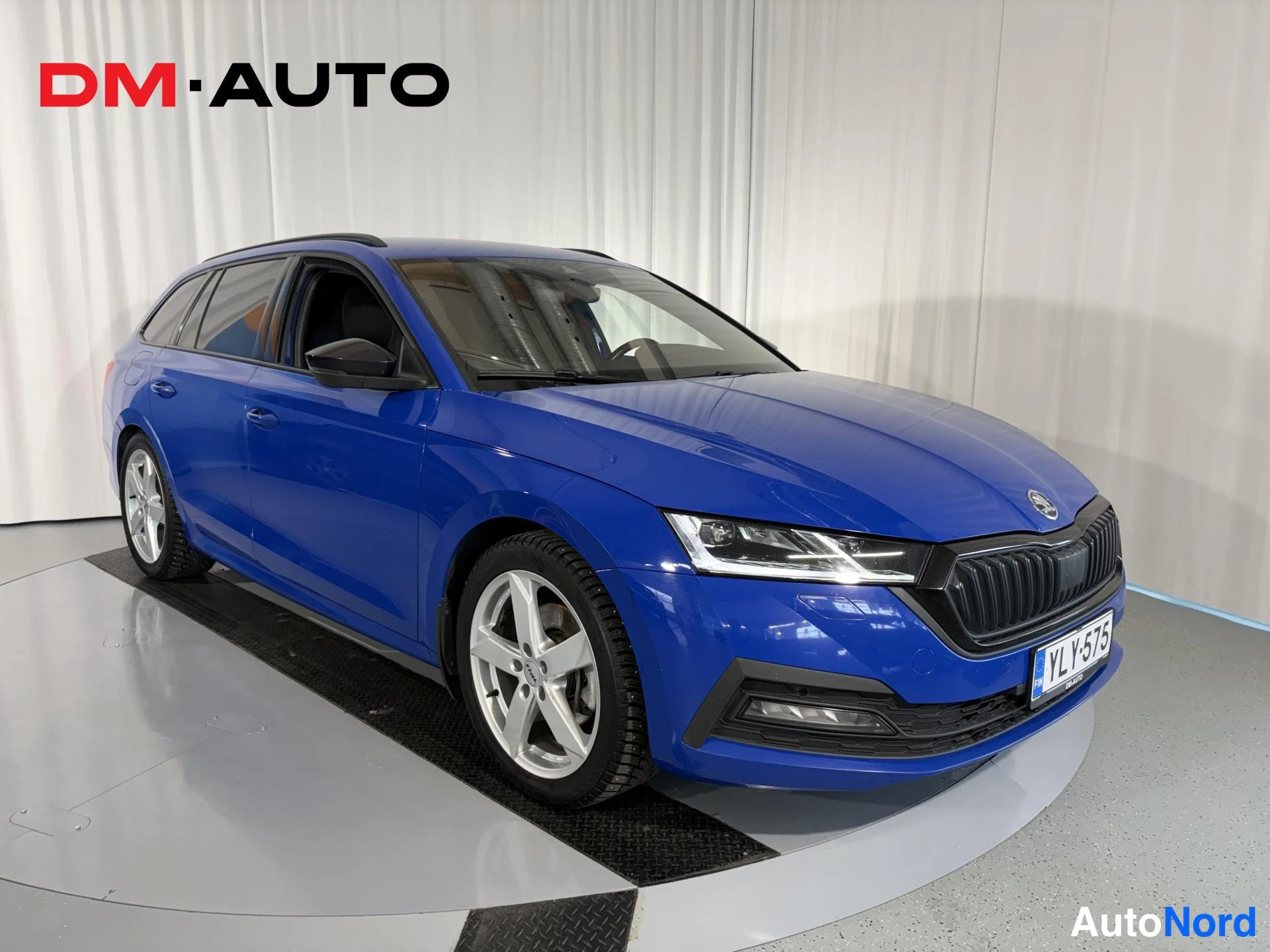 Etuviisto, nokka oikealle: Sininen Skoda Octavia Combi kolmeneljäsosan kulmakuvassa keula oikealla, hopeavanteet ja rekisterikilpi näkyvissä.