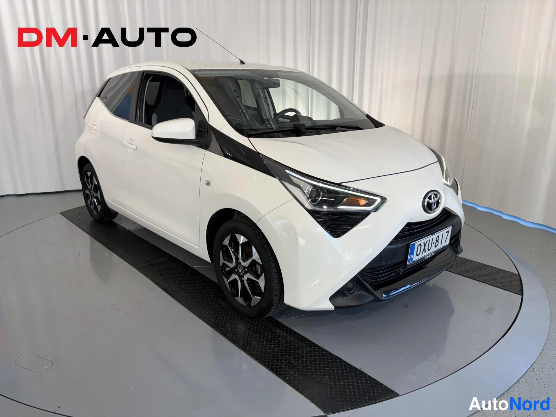 Etuviisto, nokka oikealle: Valkoinen Toyota Aygo -henkilöauto etuviistosta oikealta, rekisteritunnus, mustat kevytmetallivanteet.