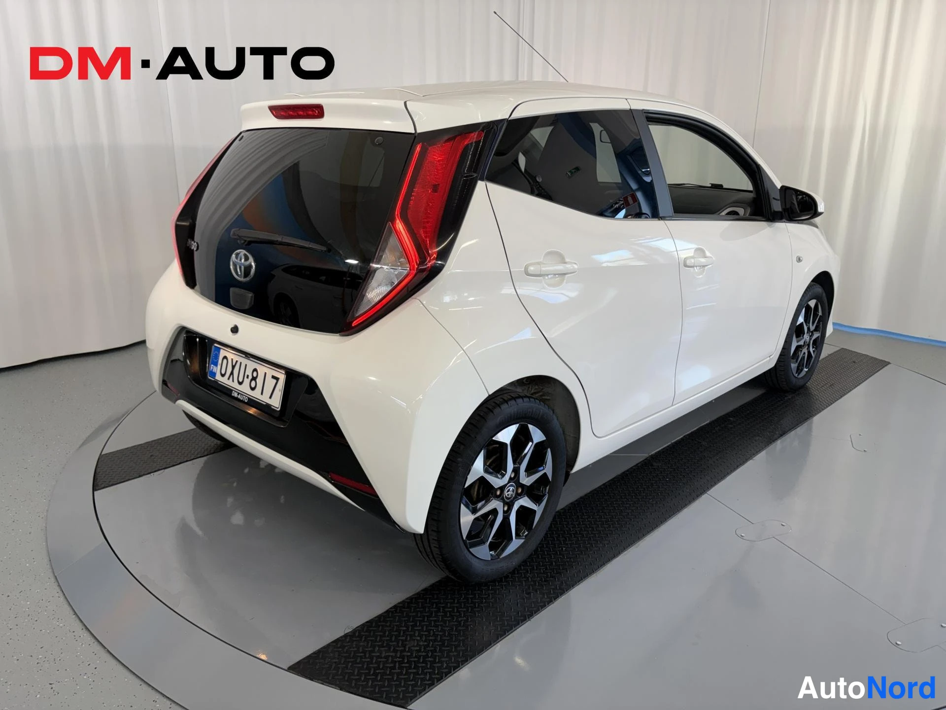 Takaviisto: Auton takakulma vasemmalta: valkoinen Toyota Aygo, musta takaluukku, Toyota-merkki ja rekisteritunnus.