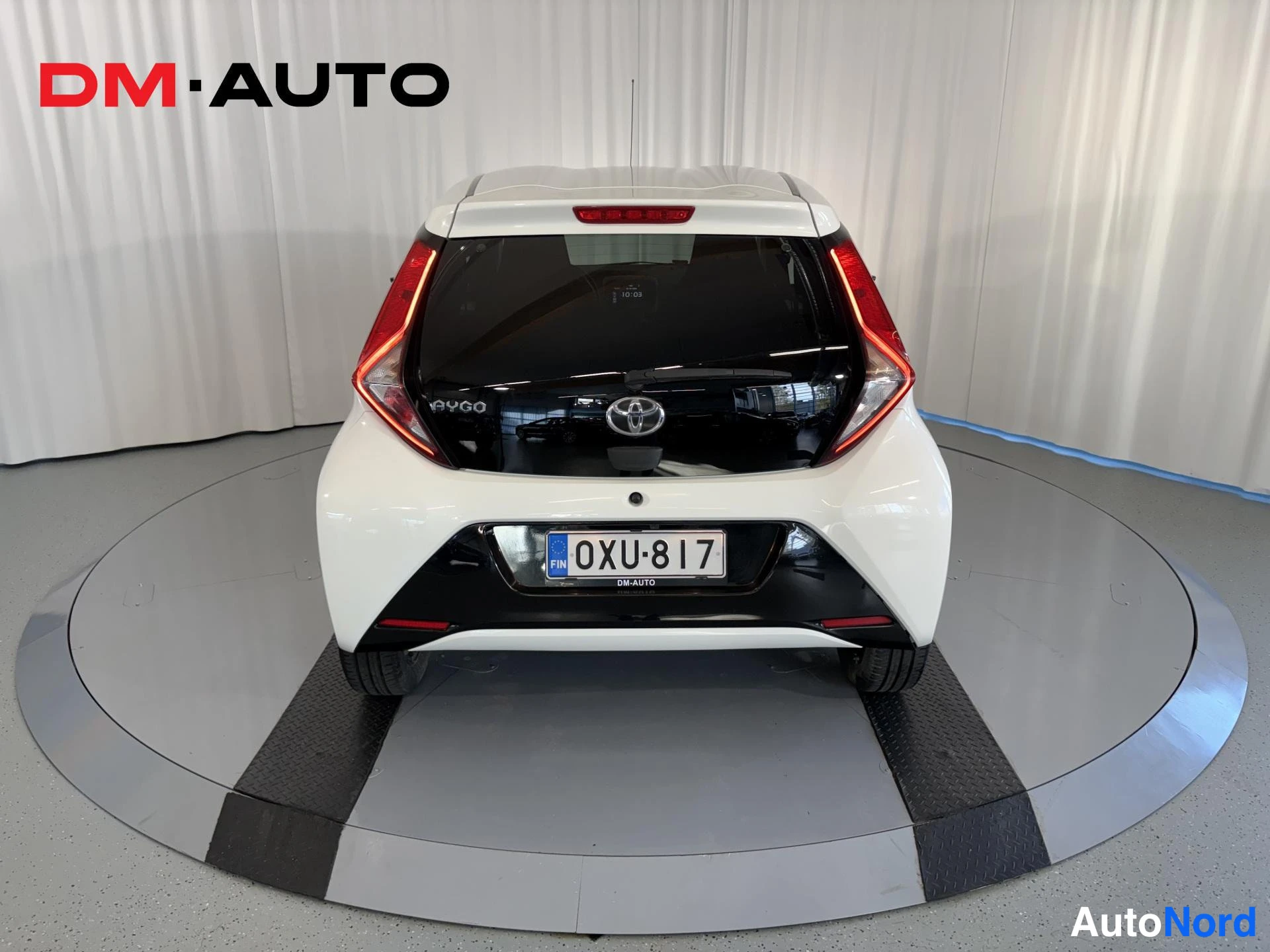Takaa: Auton takaapäin: valkoinen Toyota Aygo, musta takaluukku Aygo-tekstillä, Toyota-merkki ja rekisteritunnus.