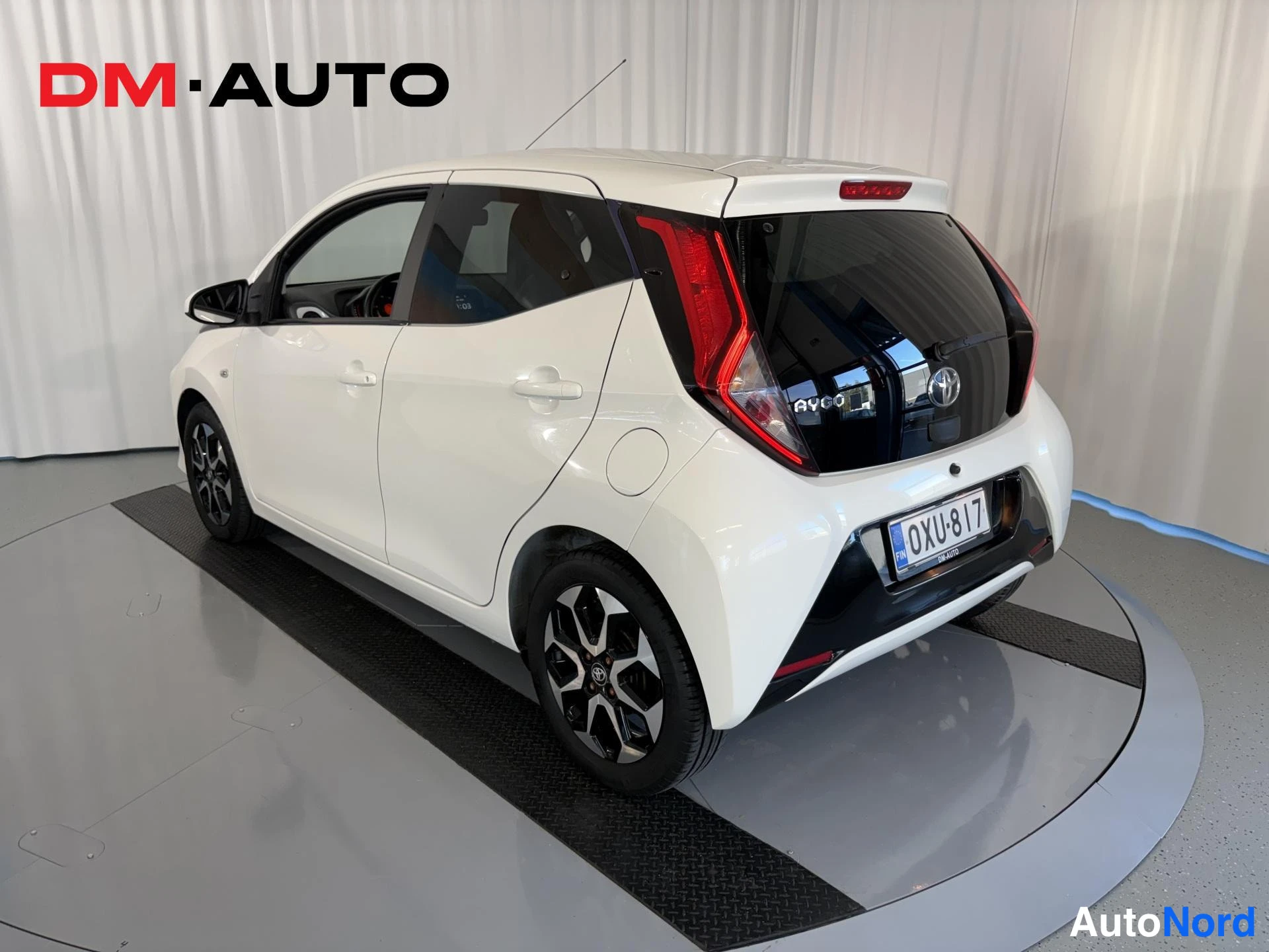 Takaviisto: Auton takakulma oikealta: valkoinen Toyota Aygo, musta takaluukku, Toyota-merkki ja rekisteritunnus.