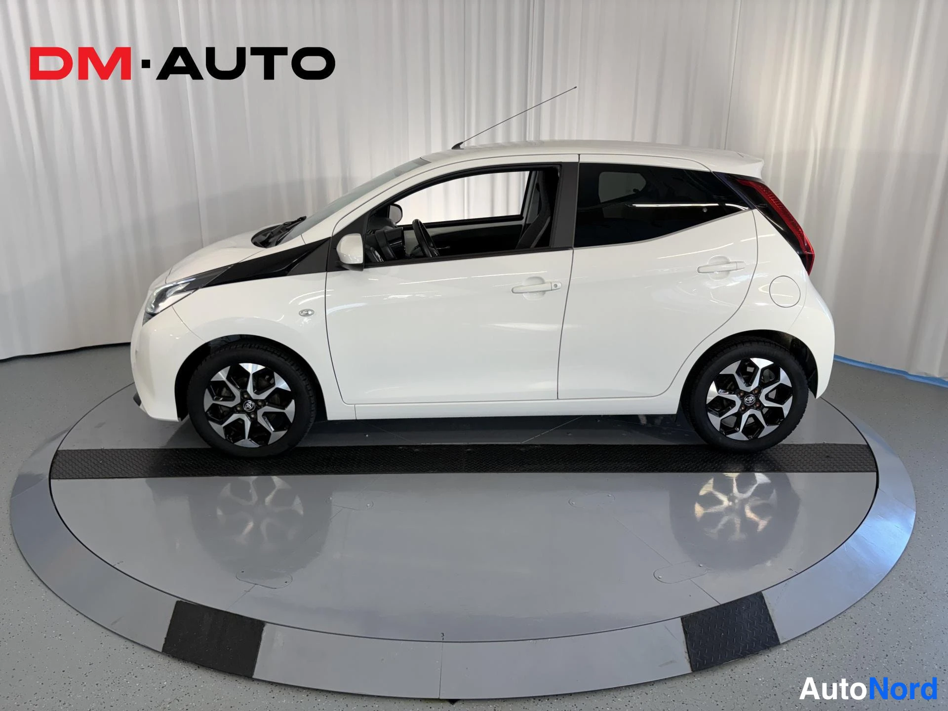 Sivulta: Auton sivukuva oikealta: valkoinen Toyota Aygo, viisiovea ja tummat kevytmetallivanteet.
