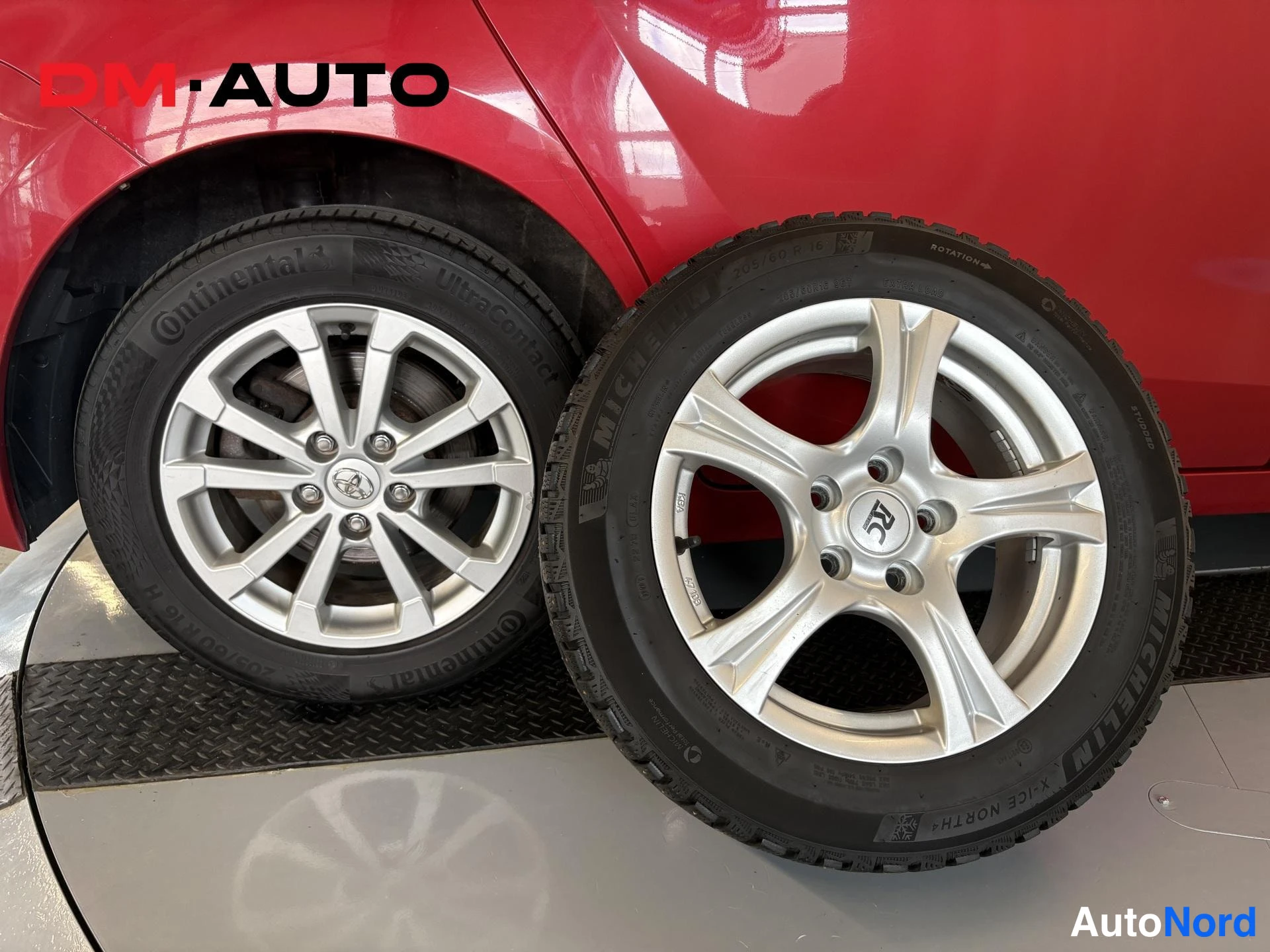 Muu: Kaksi kesärenkavannettä punaisen auton kyljen vieressä: toisessa Continental-rengas ja hopea Toyota-vante, toisessa Michelin X-ICE NORTH -rengas hopeisella viis
