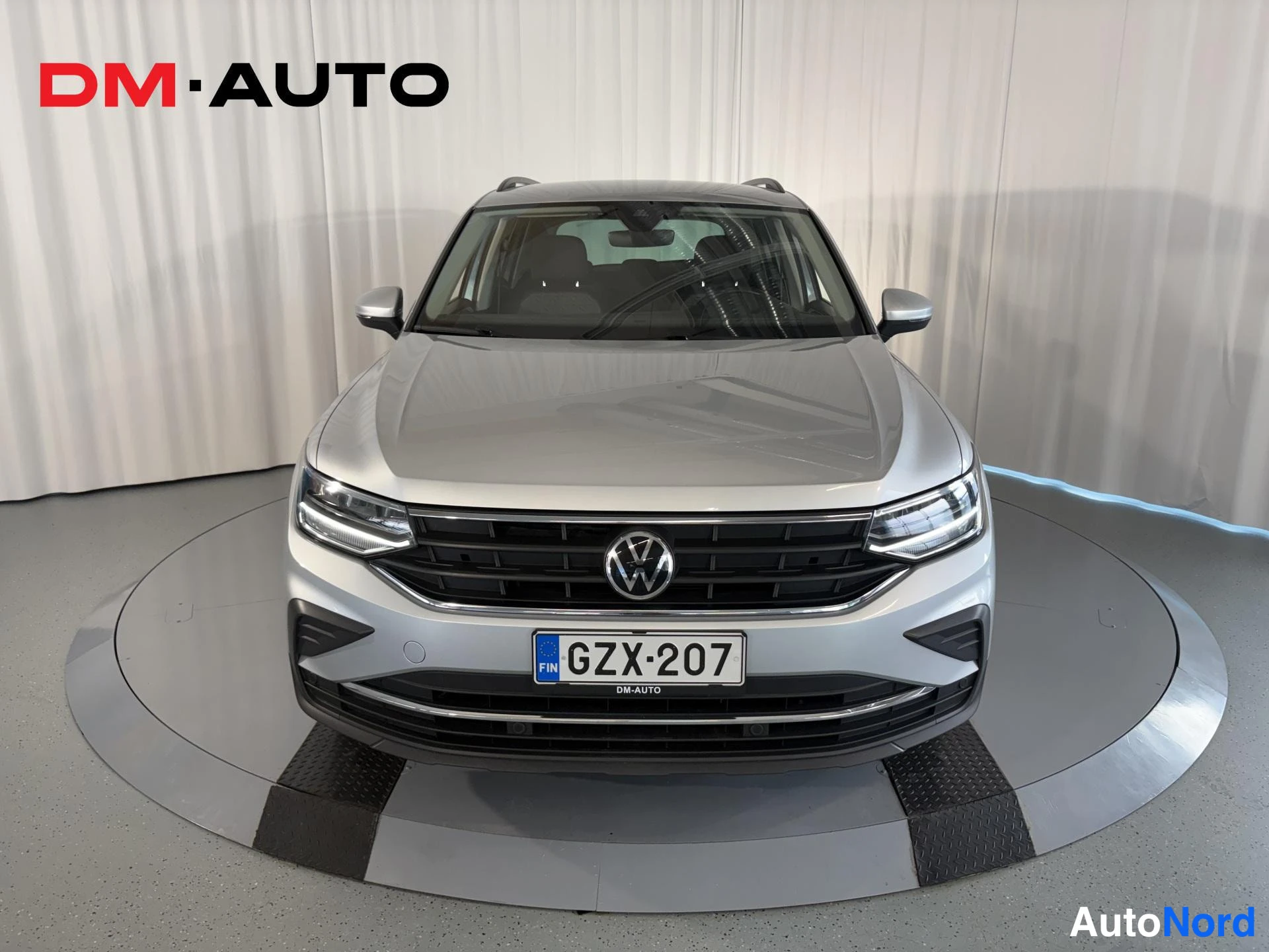 Edestä: Hopeanvärinen Volkswagen Tiguan suoraan edestä kuvattuna sisätiloissa alustalla.