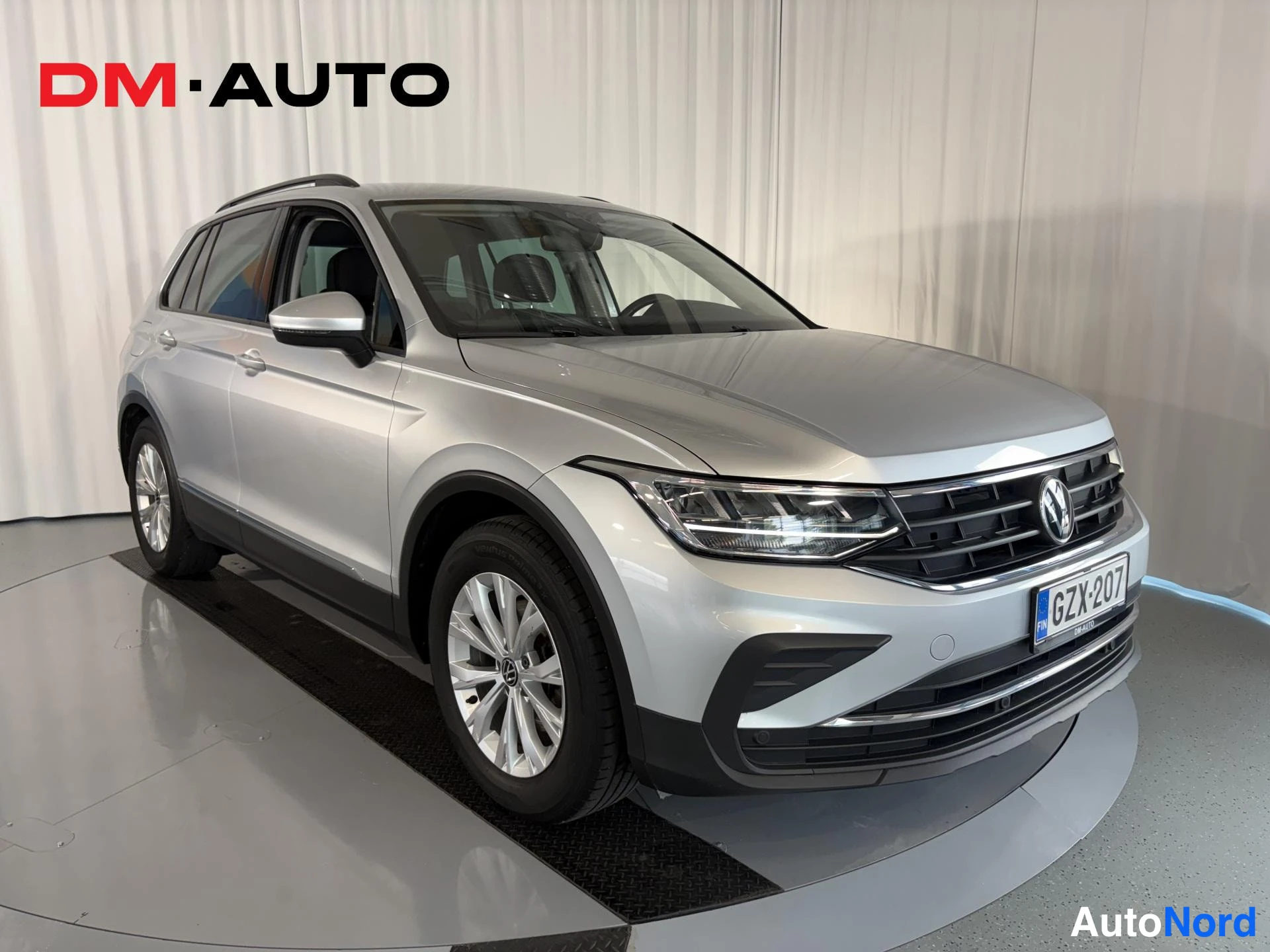 Etuviisto, nokka oikealle: Hopeanvärinen Volkswagen Tiguan edestä oikealta kuvattuna sisätiloissa alustalla.